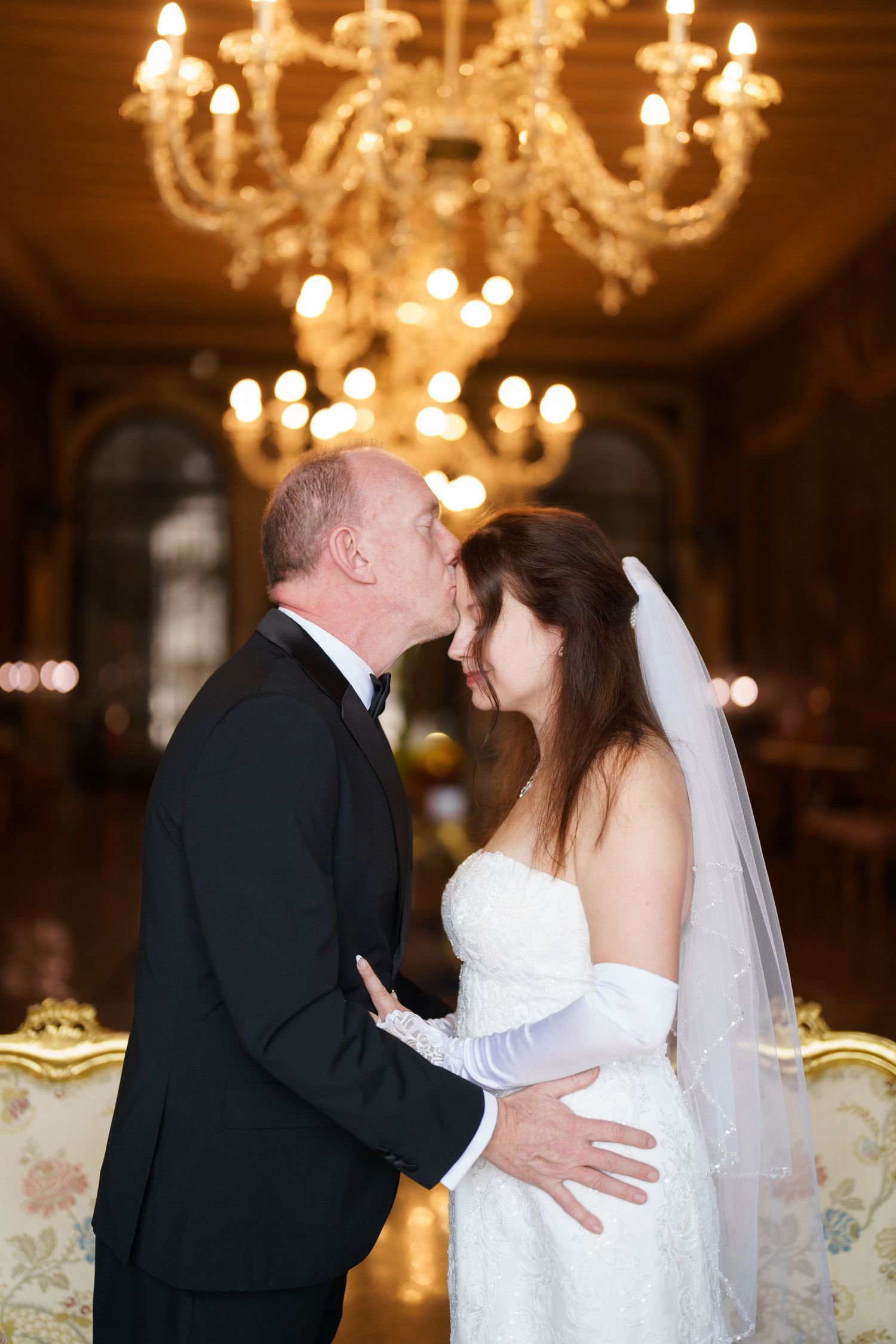 A bride and groom share their first dance under elegant crystal chandeliers in an opulent ballroom.