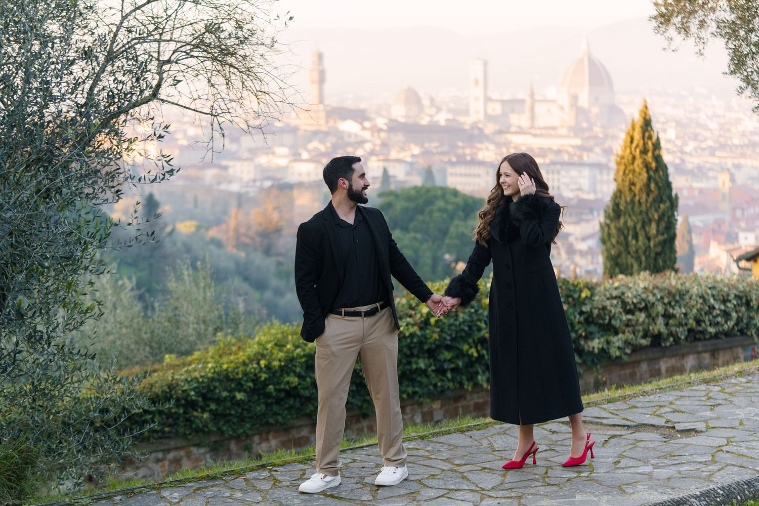 A couple walks together along a scenic overlook path with a cityscape view in the background.