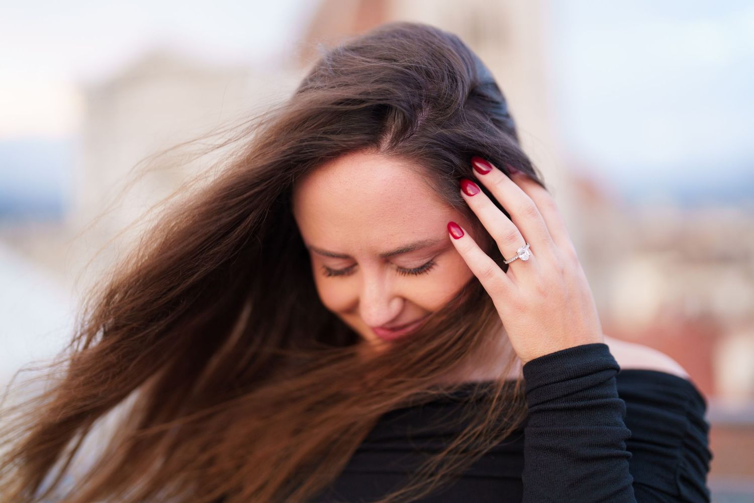 A person with long dark hair holds their head in distress while sitting against a blurred background.