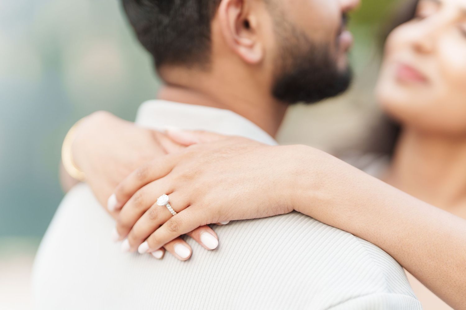 Close up of hands embracing with diamond engagement ring visible on woman's finger during romantic moment.