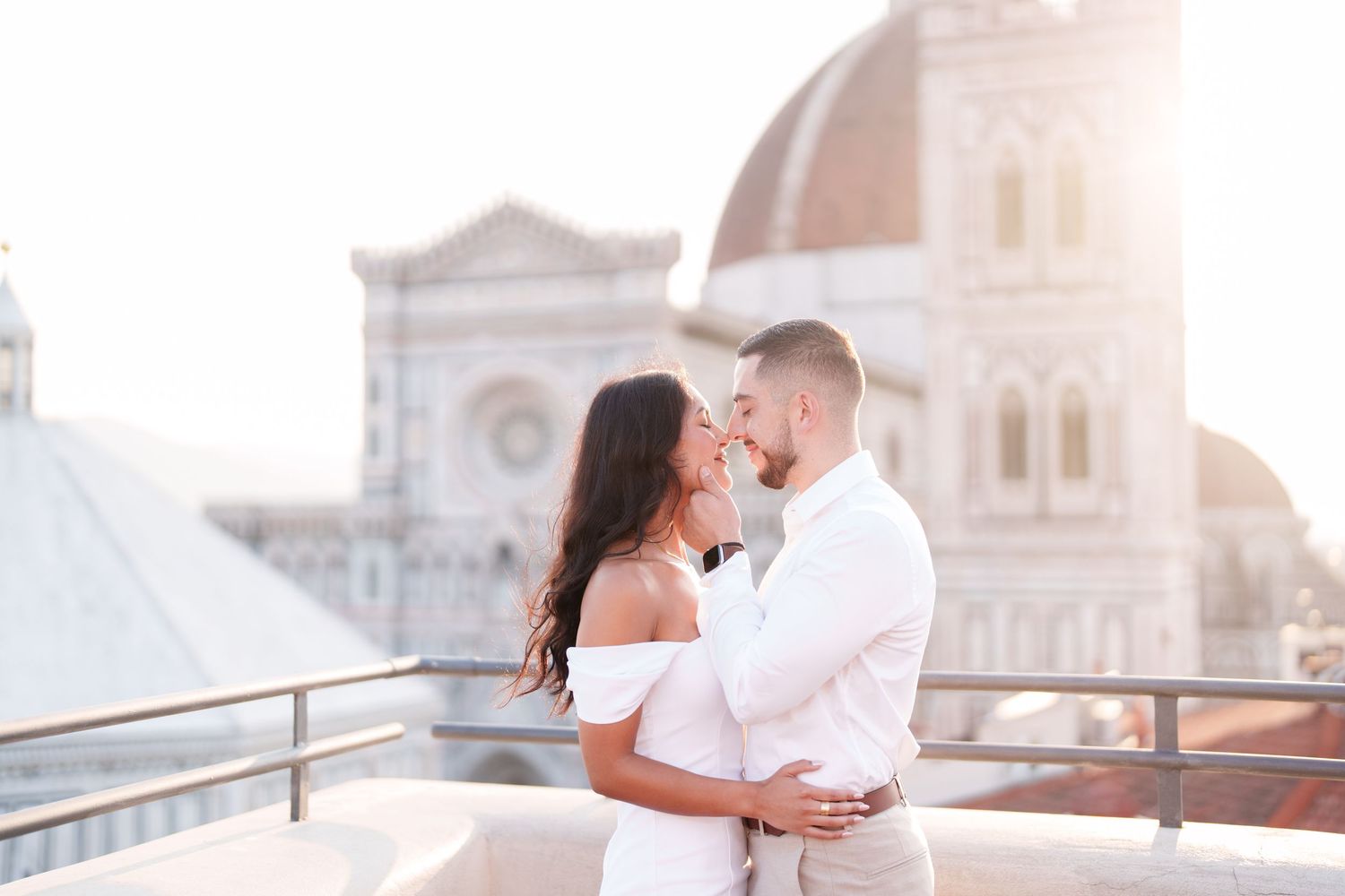 A romantic couple embraces on a rooftop terrace with Florence Cathedral's iconic dome in the background at sunset.