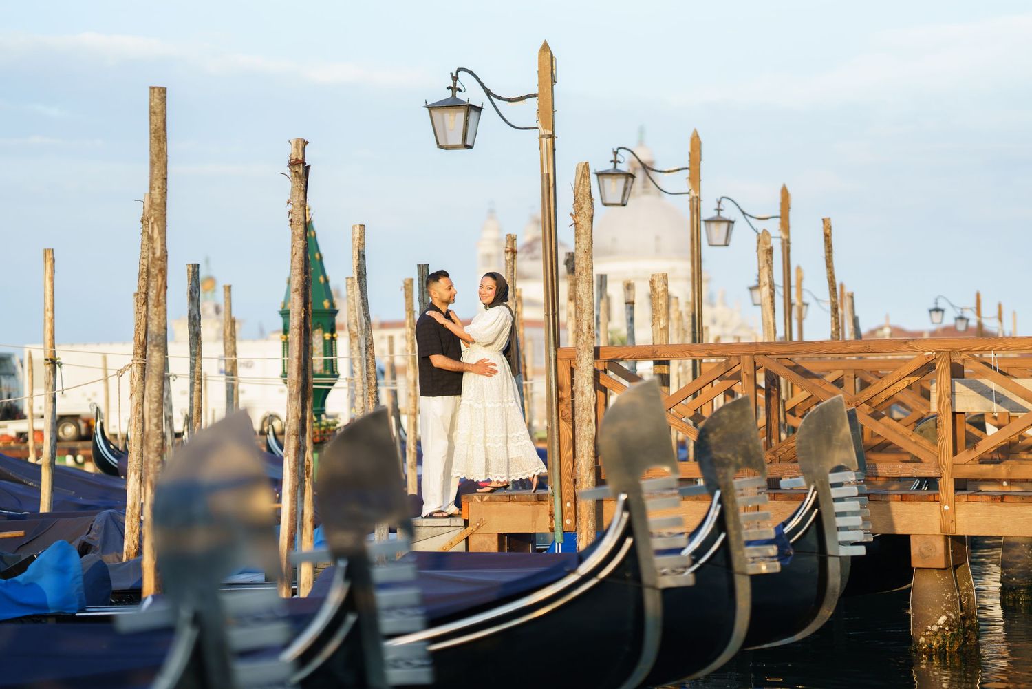 Couple embracing on Venice dock surrounded by gondolas with San Giorgio Maggiore church in background.