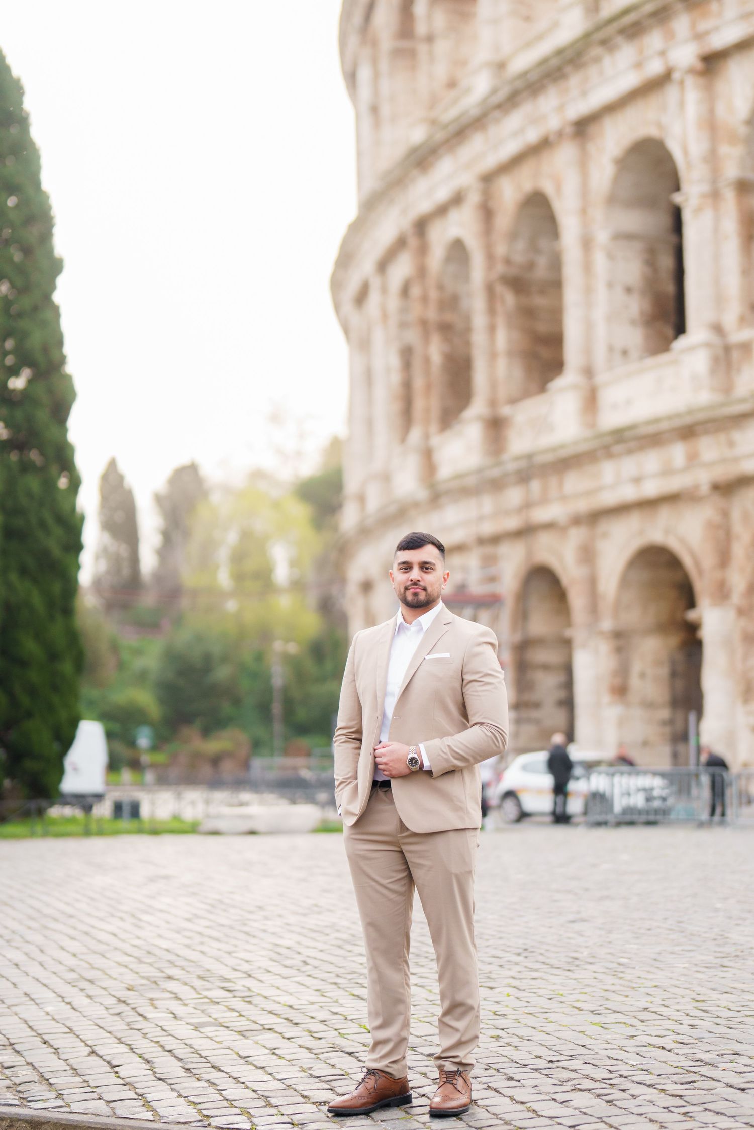 Man in beige suit posing confidently in front of the Colosseum in Rome, Italy on a bright day.