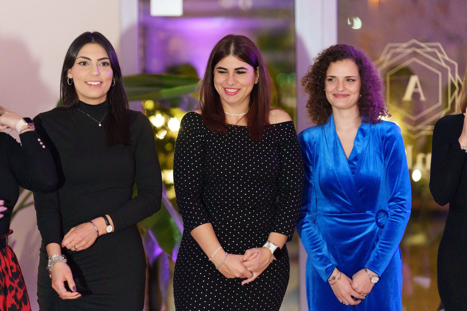 Four women posing together at an elegant indoor event, wearing formal attire including black and blue outfits.