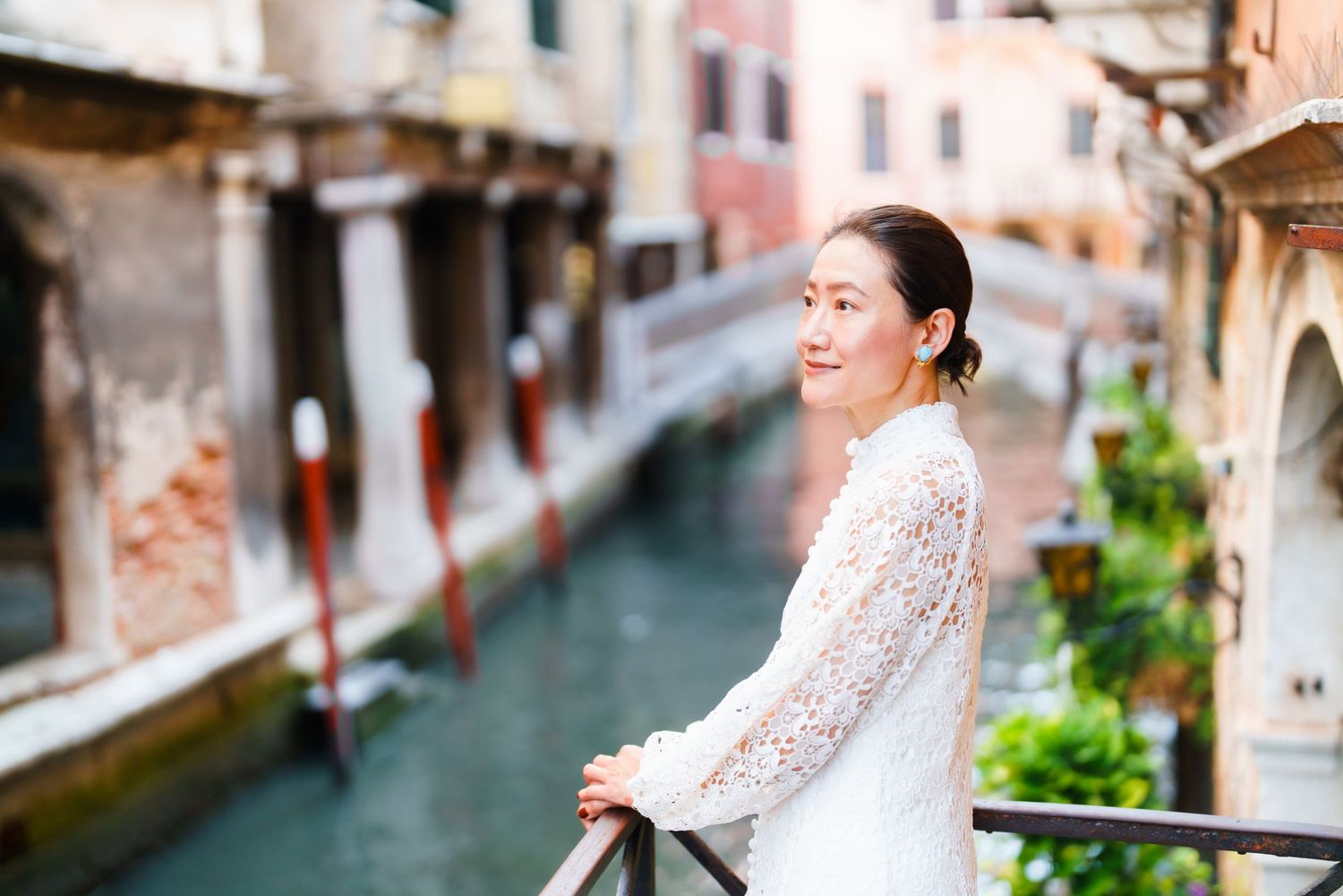 Woman in white lace sweater smiling on a bridge overlooking a scenic Venice canal.
