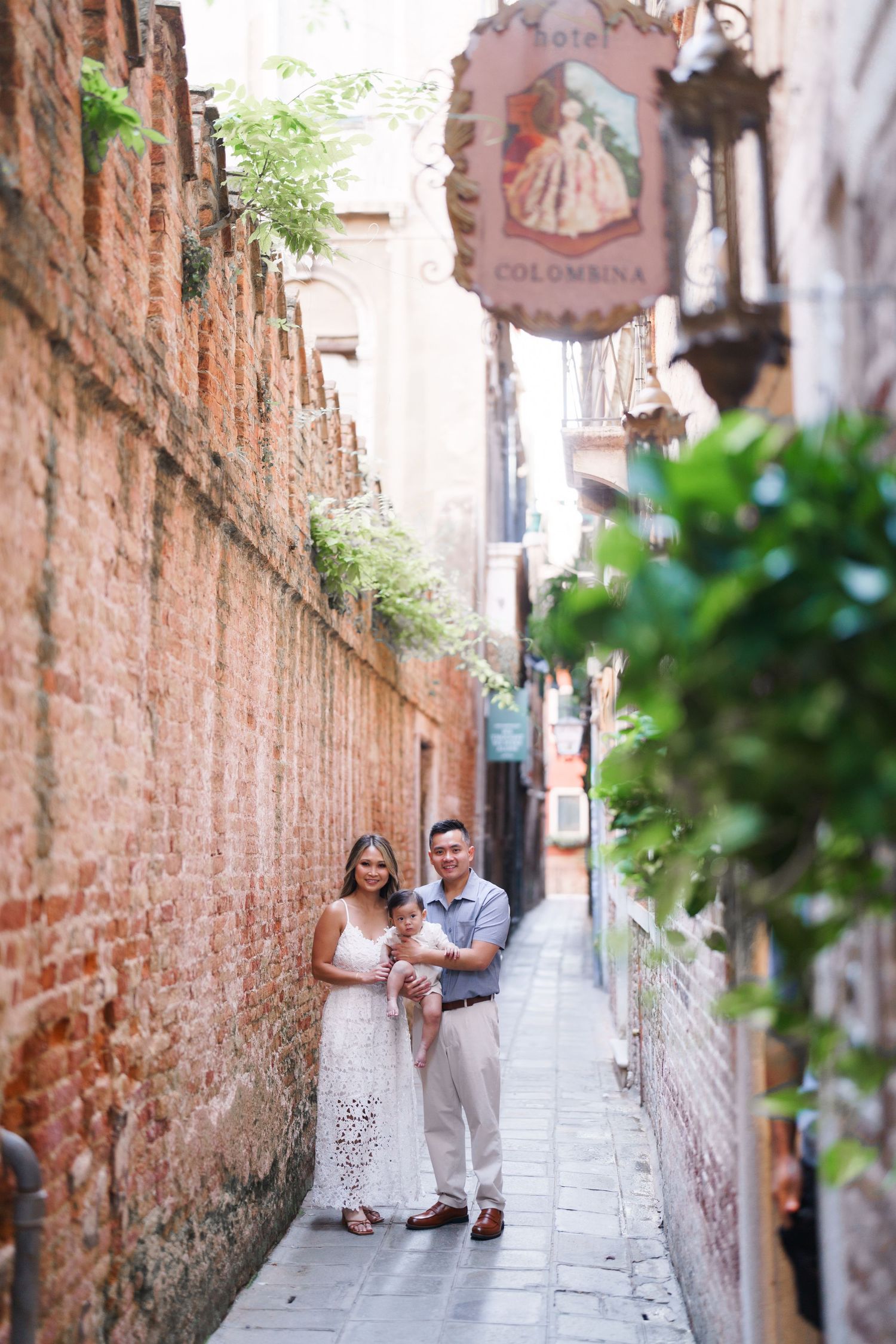 Family posing in a narrow Venice alley with brick walls and Hotel Colombina sign overhead.