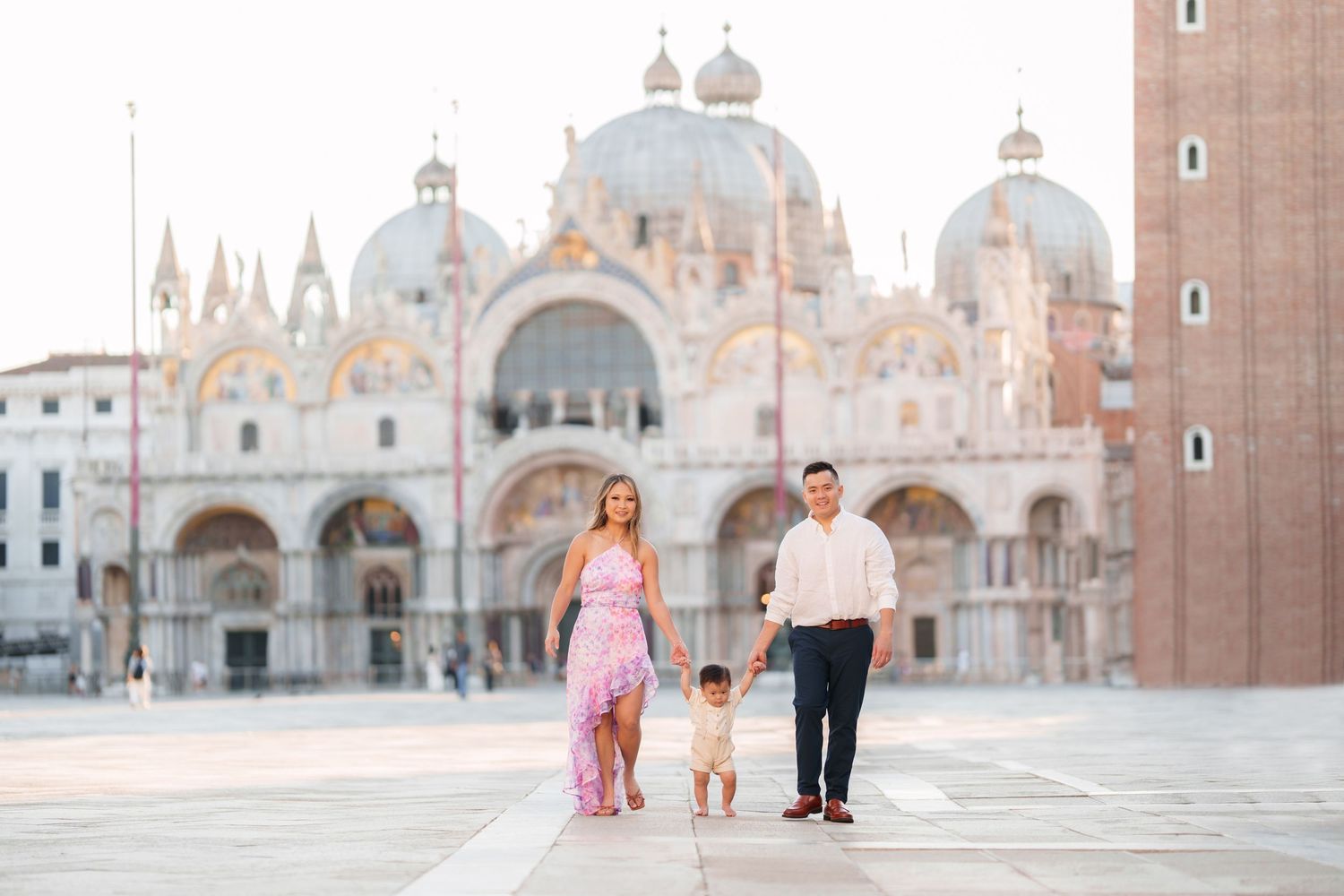 Family of three posing in St. Mark's Square, Venice, with the iconic Basilica di San Marco in the background.