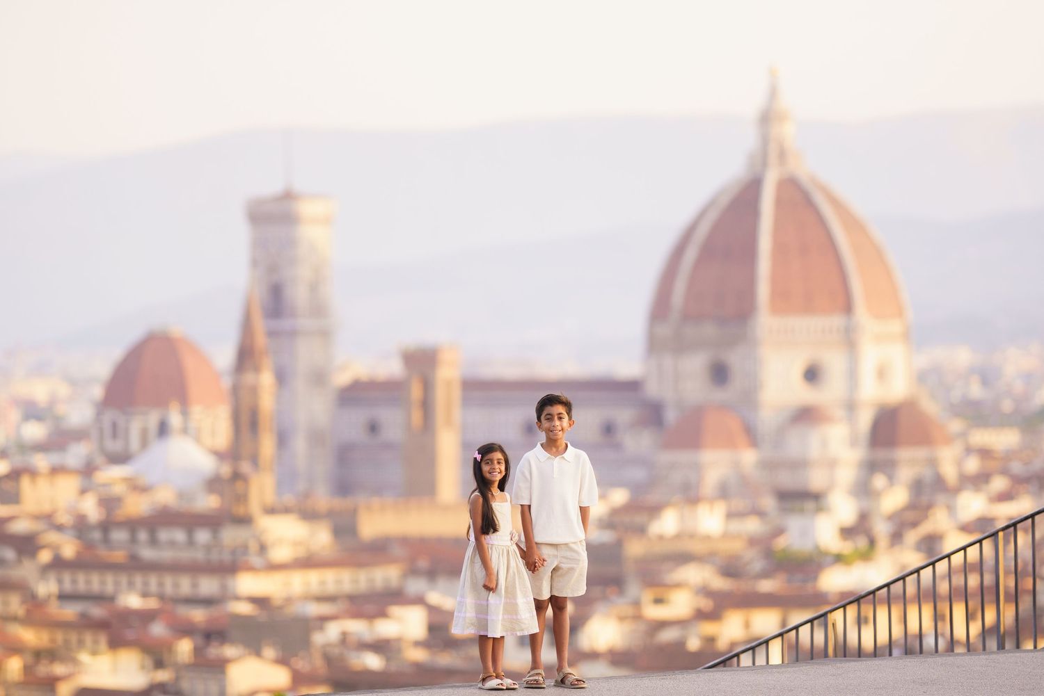 Two children posing together on a terrace overlooking Florence skyline with the iconic Duomo cathedral in the background.