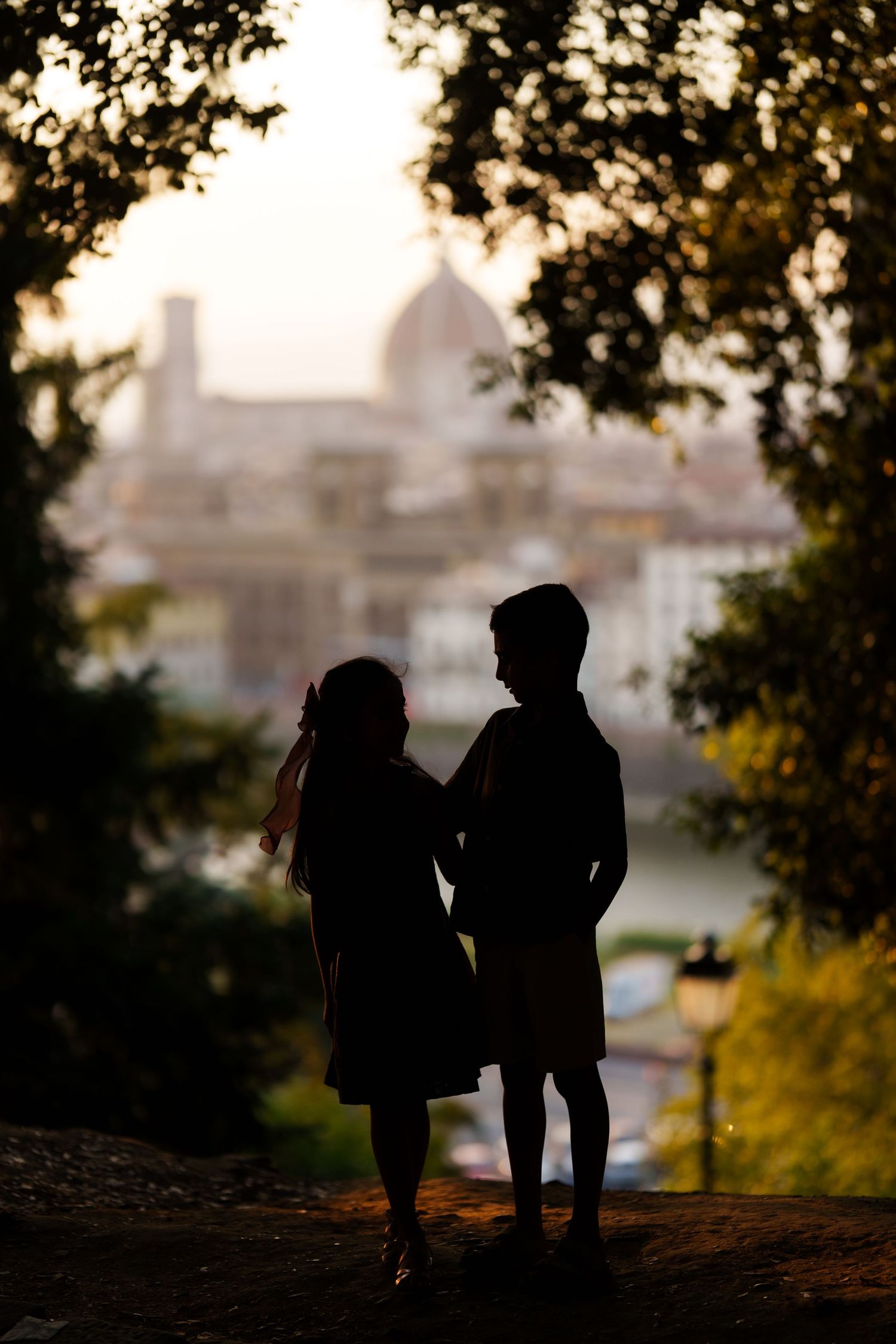 Silhouette of a romantic couple standing together at sunset with Florence cathedral dome visible in background.