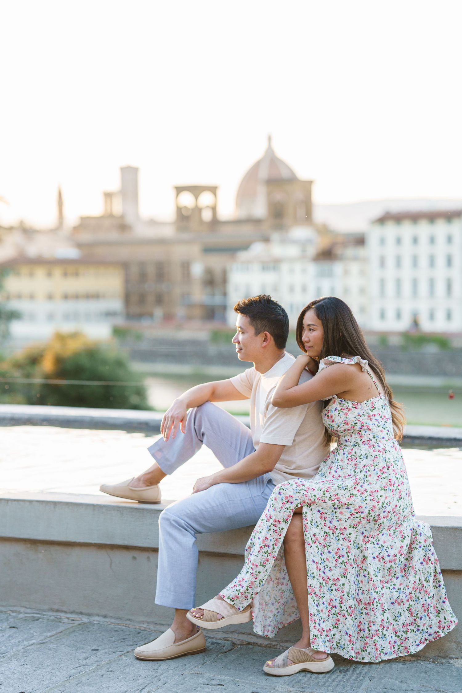 Couple sitting on a ledge with Florence skyline and cathedral dome in the background at sunset.
