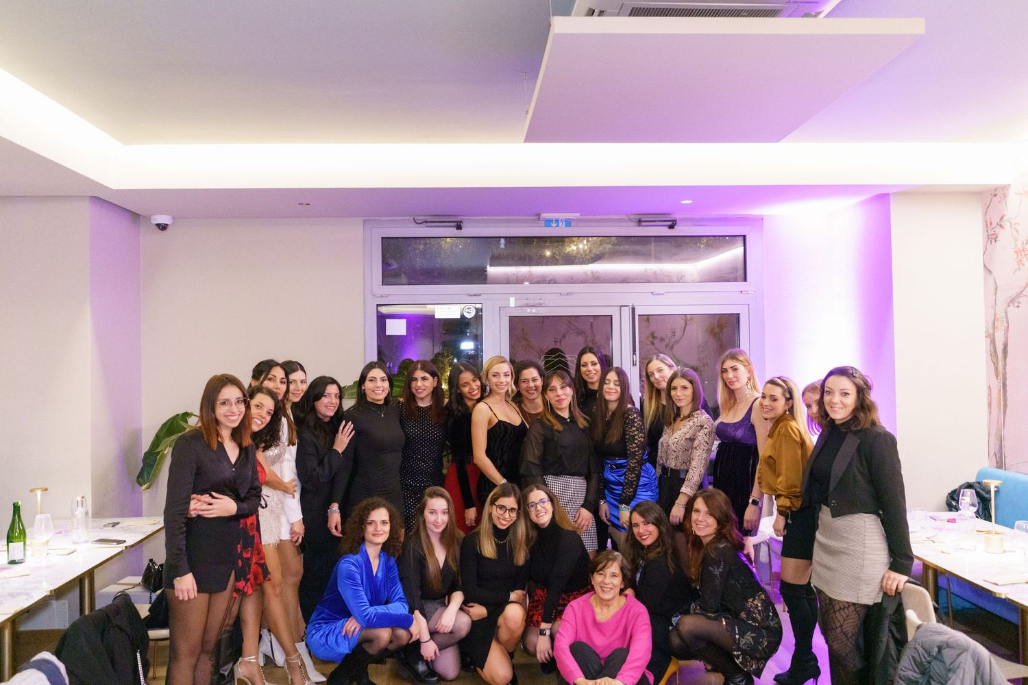 Large group of women posing together at an indoor party with purple ambient lighting.