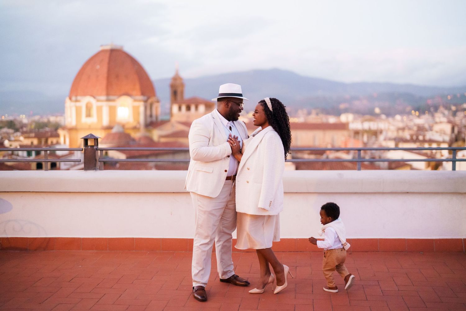 Family in white attire poses on Florence rooftop with Duomo cathedral dome at dusk.
