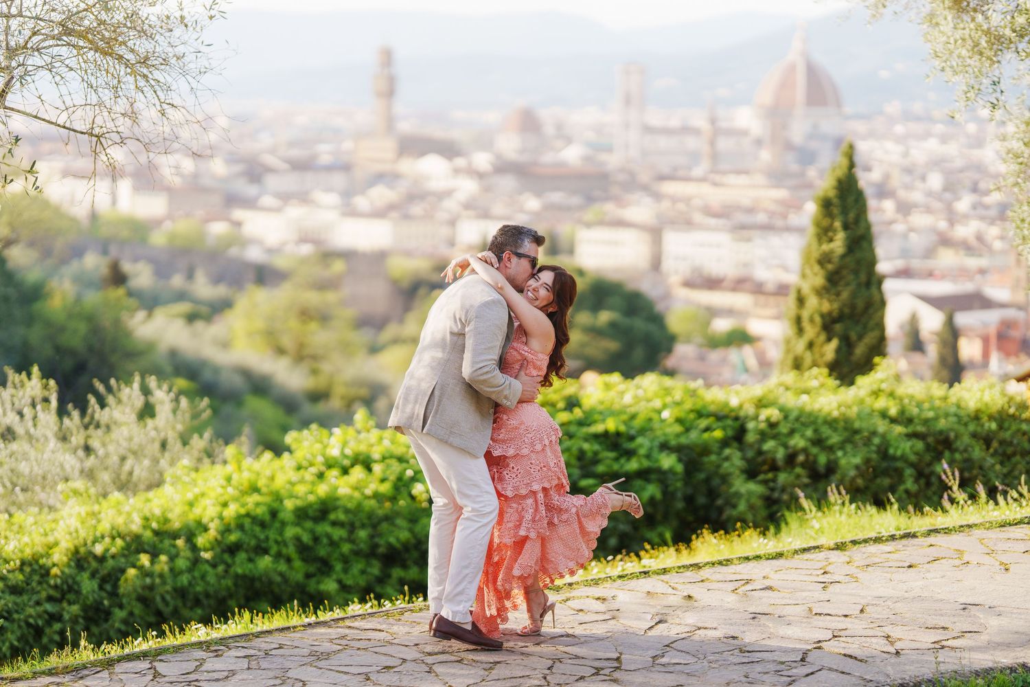 Romantic couple embraces while overlooking a scenic Italian cityscape with historic architecture and rolling hills.