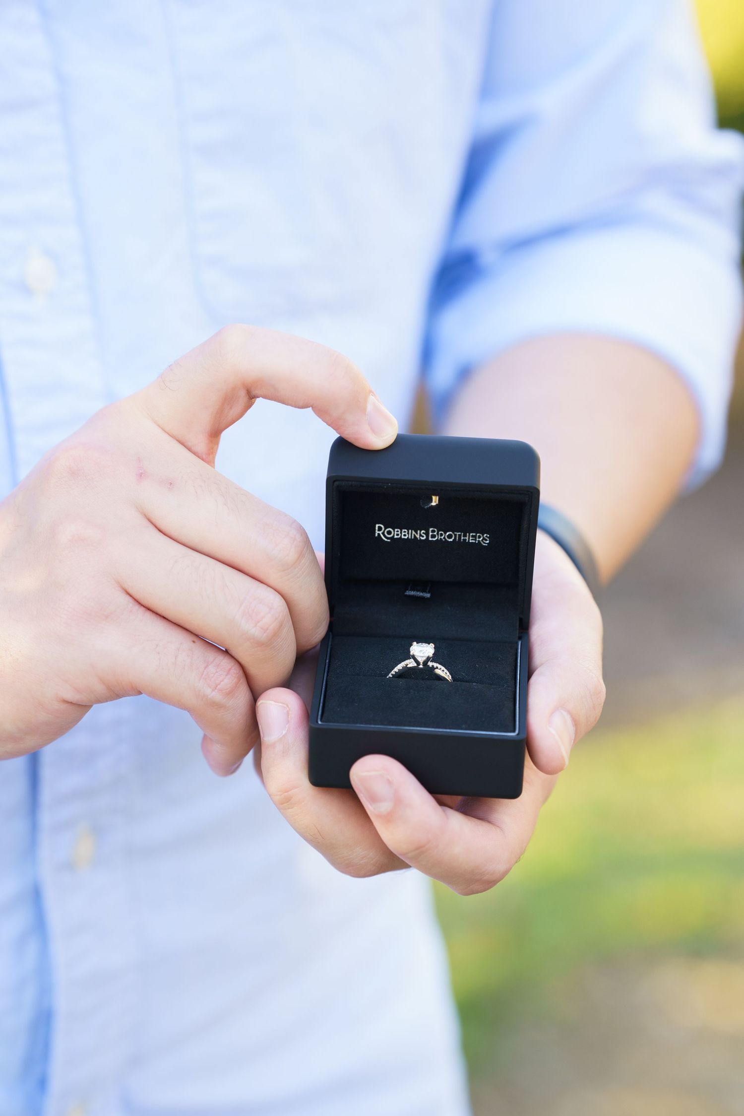 Hands hold a small black engagement ring box in a sequence showing it being opened to reveal a diamond ring.