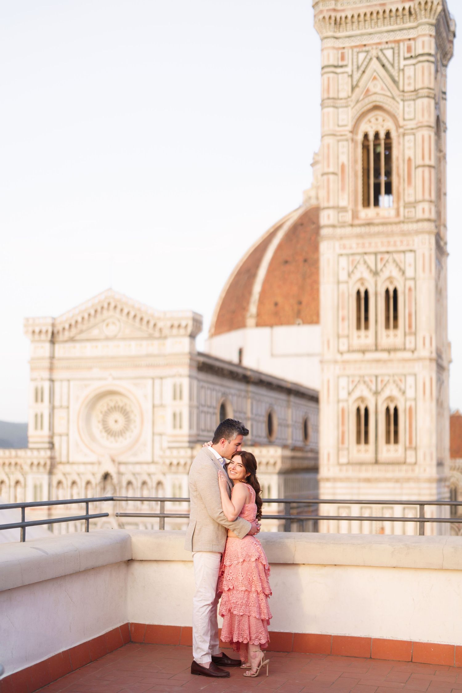 A couple embraces on a rooftop terrace with Florence's iconic Duomo cathedral and Giotto's bell tower in the background.