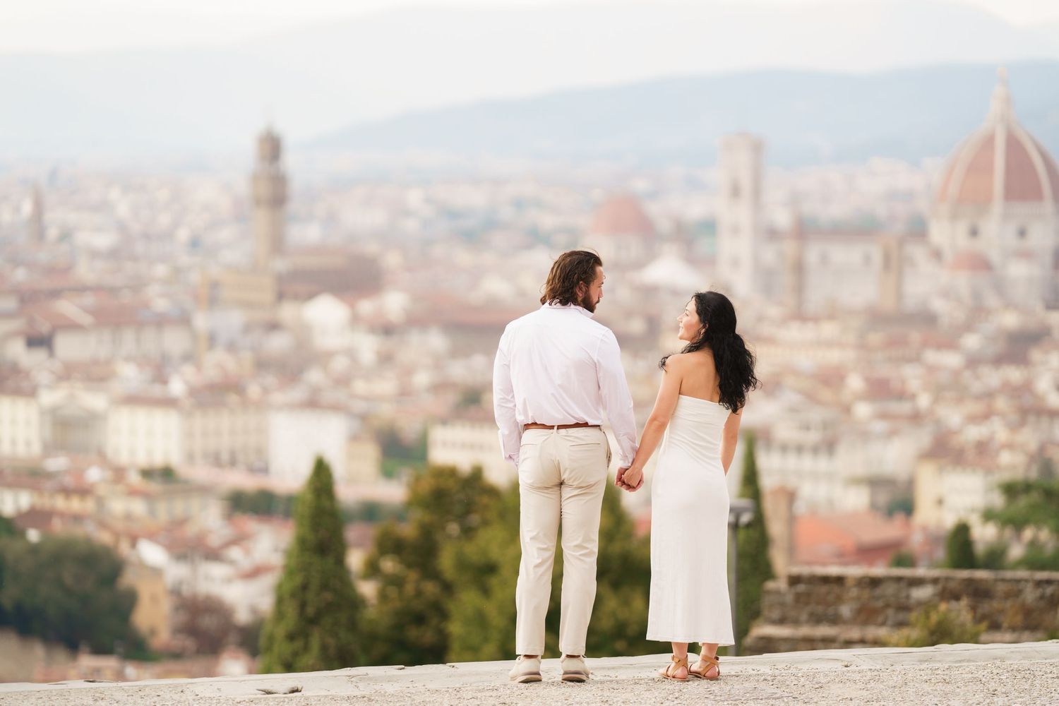 A romantic couple stands at Piazzale Michelangelo overlooking the iconic Florence cityscape with the Duomo cathedral.