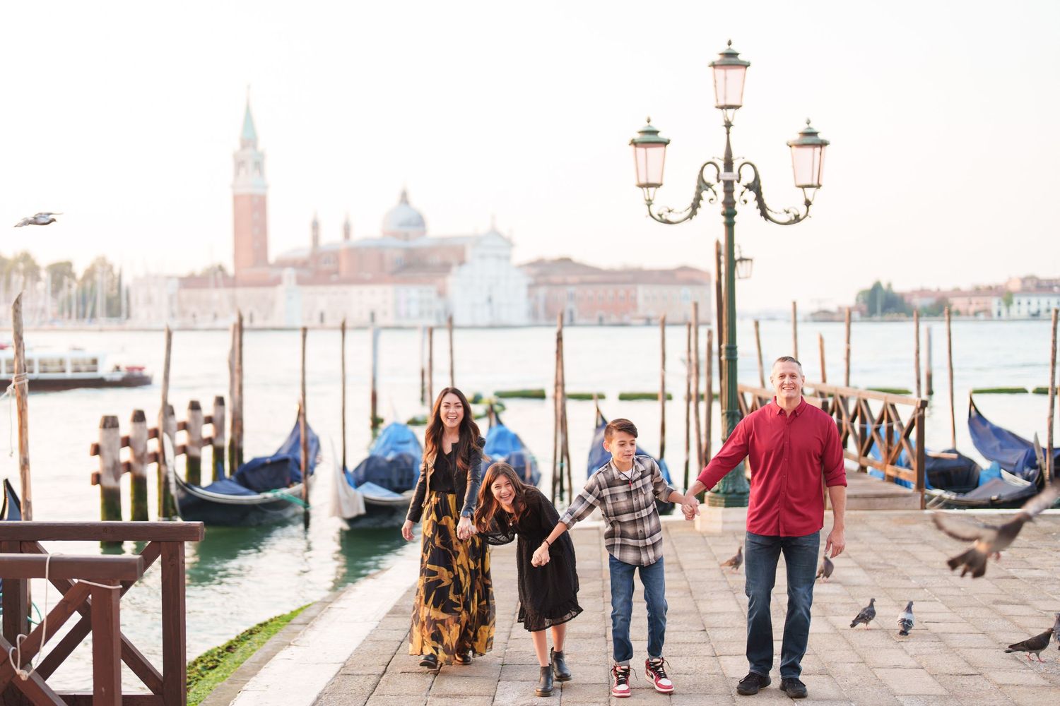 A romantic couple walking along Venice's waterfront with San Giorgio Maggiore church and gondolas in the background.