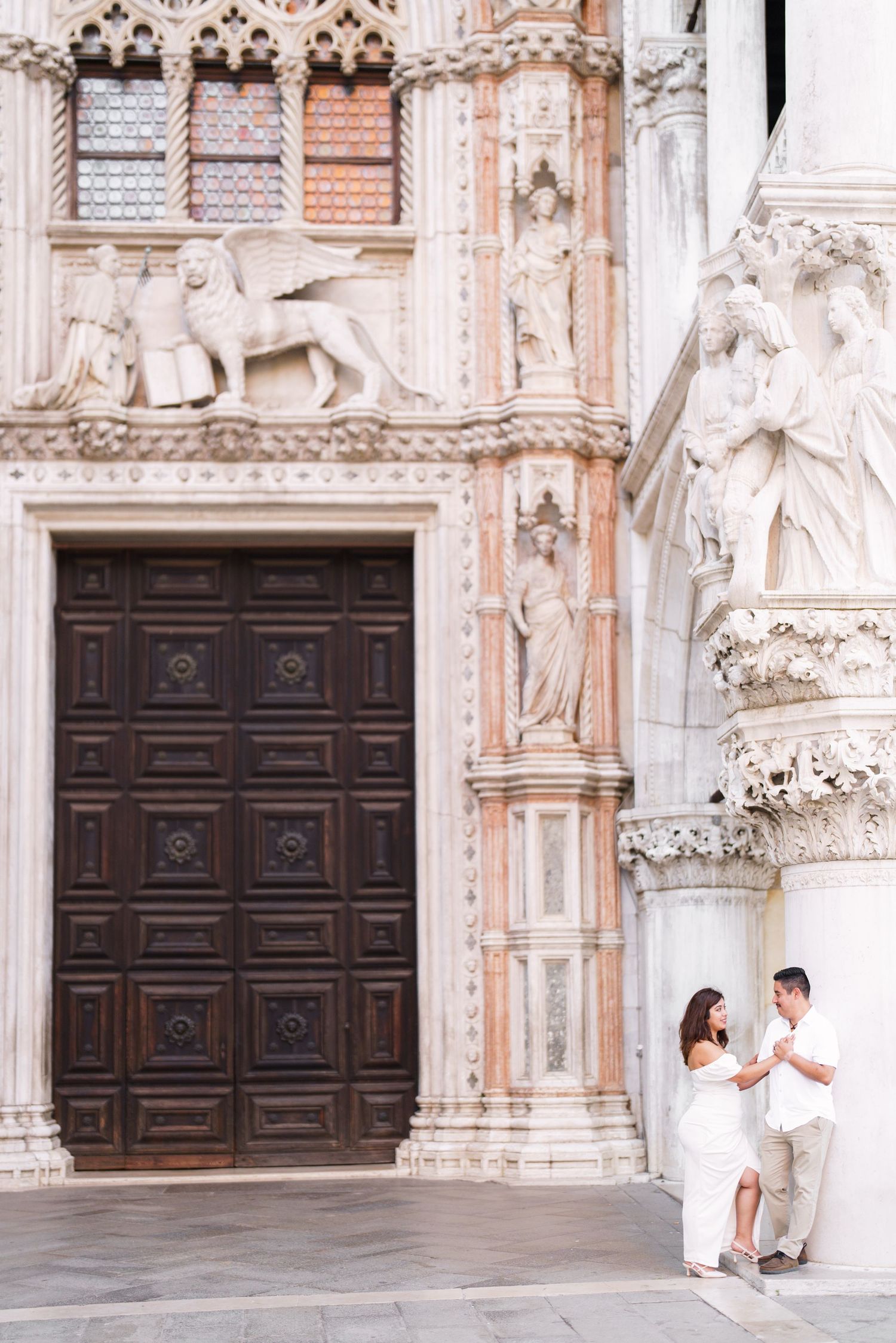 Couple shares romantic moment outside ornate cathedral doors with detailed stone carvings and architecture in Italy.