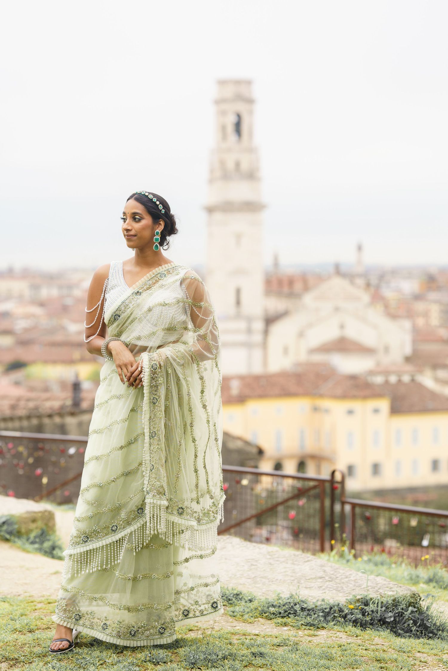 A person in a light green traditional dress poses gracefully on a hilltop overlooking an Italian cityscape with historic buildings.