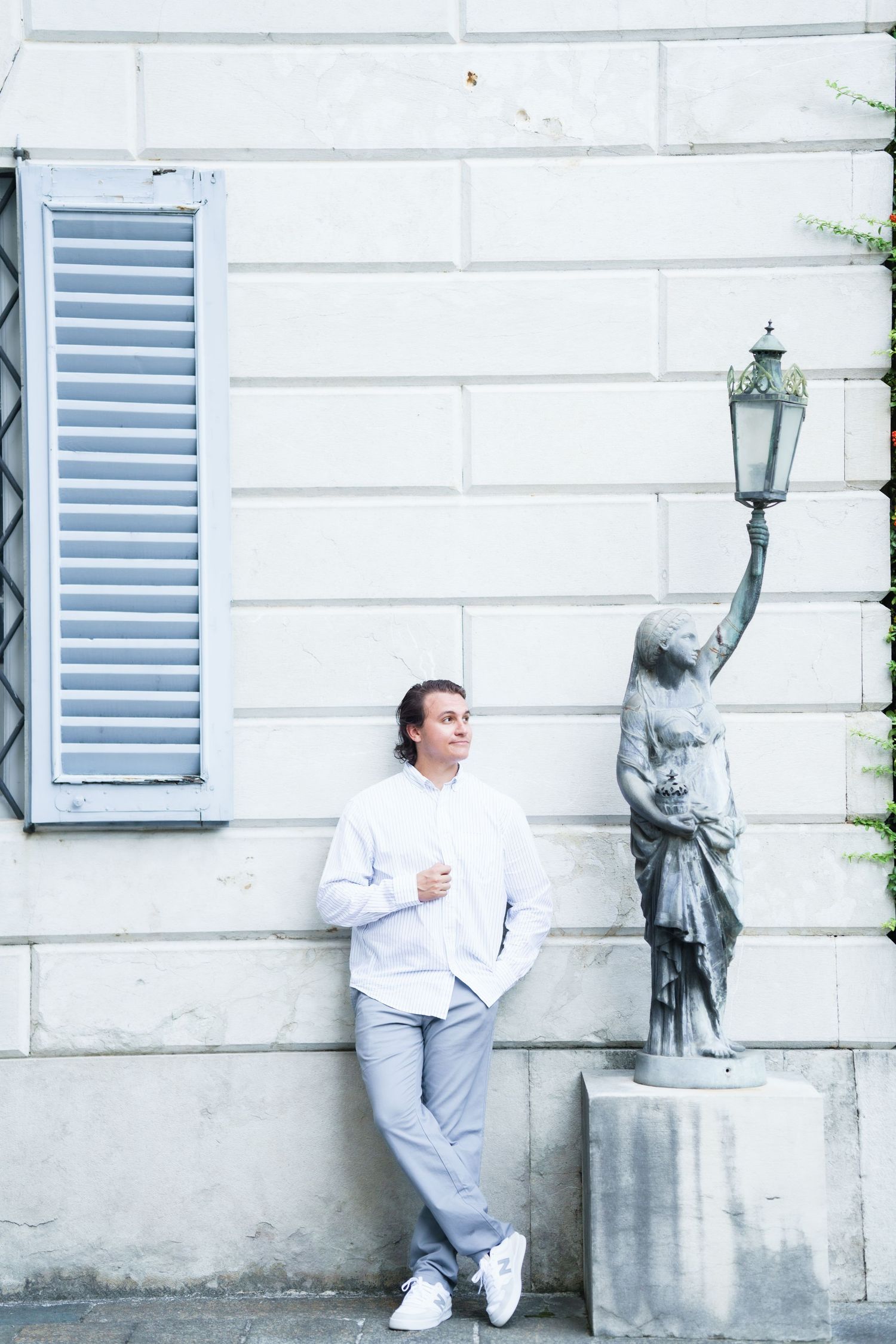 Person in white outfit poses playfully with stone statue on building wall in sequential photos.