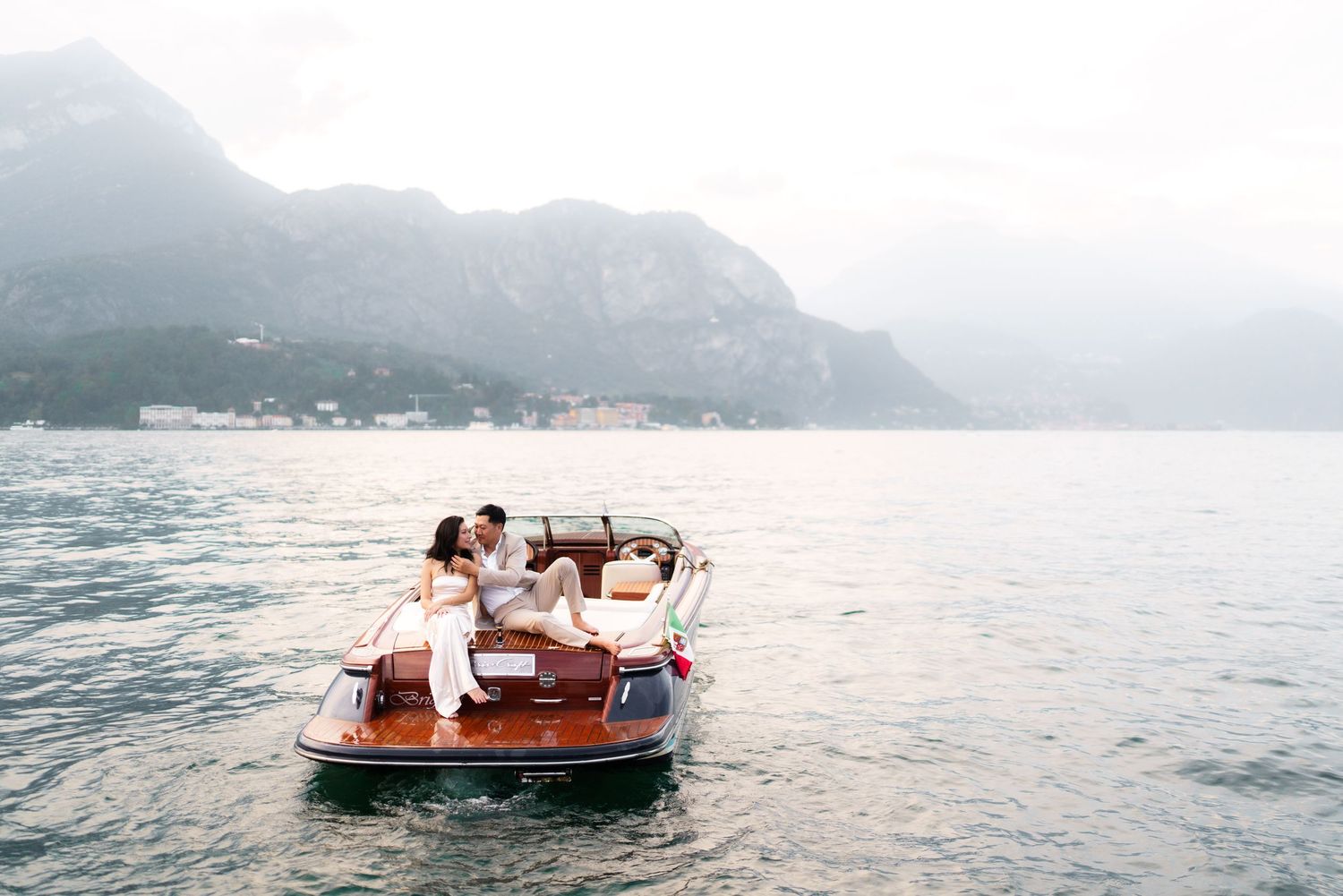 Vintage wooden boat gliding across misty lake waters with mountains in the background.