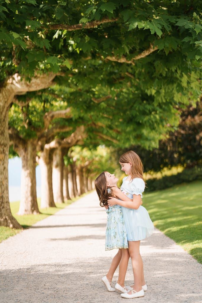 Two young children share a sweet moment while playing together on a scenic tree-lined path.