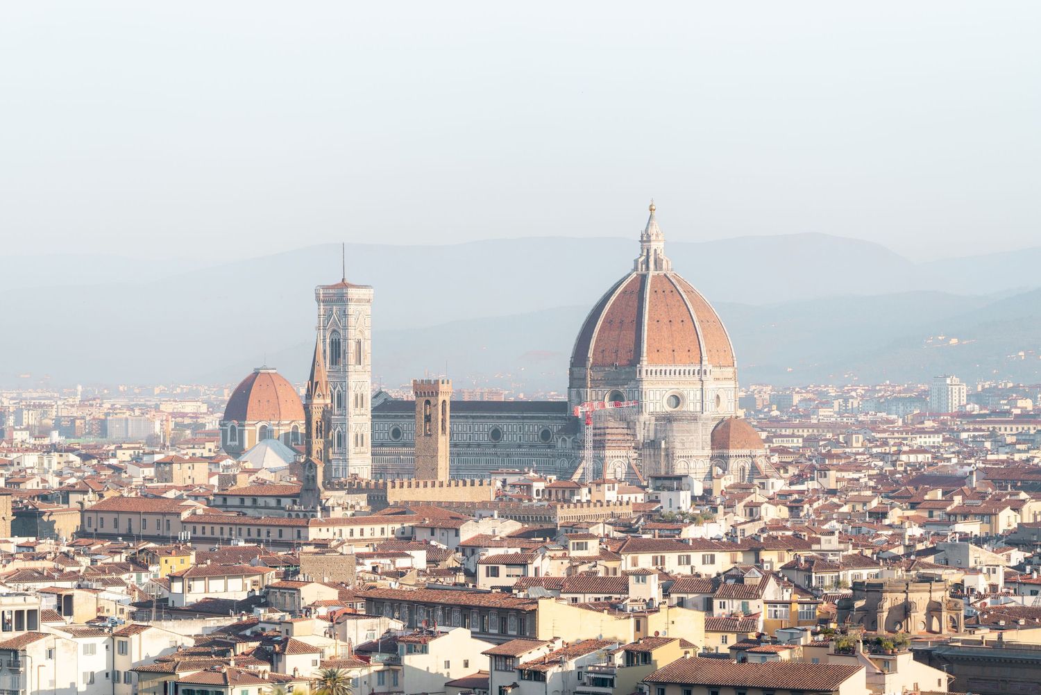 Aerial view of Florence's iconic Duomo cathedral dome and cityscape against misty mountains in Italy.