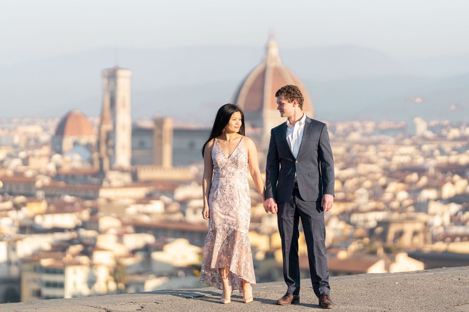 A couple stands together overlooking the historic skyline of Florence, Italy with the Duomo cathedral in the background.