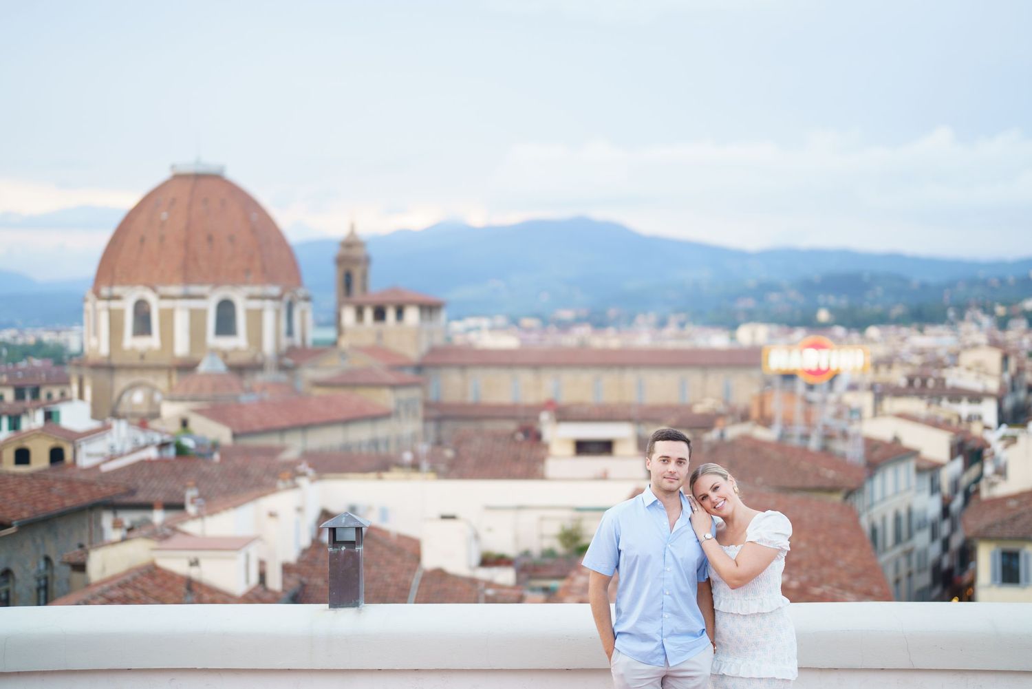 Panoramic view of Florence cityscape with historic domed buildings and terracotta rooftops against mountain backdrop.