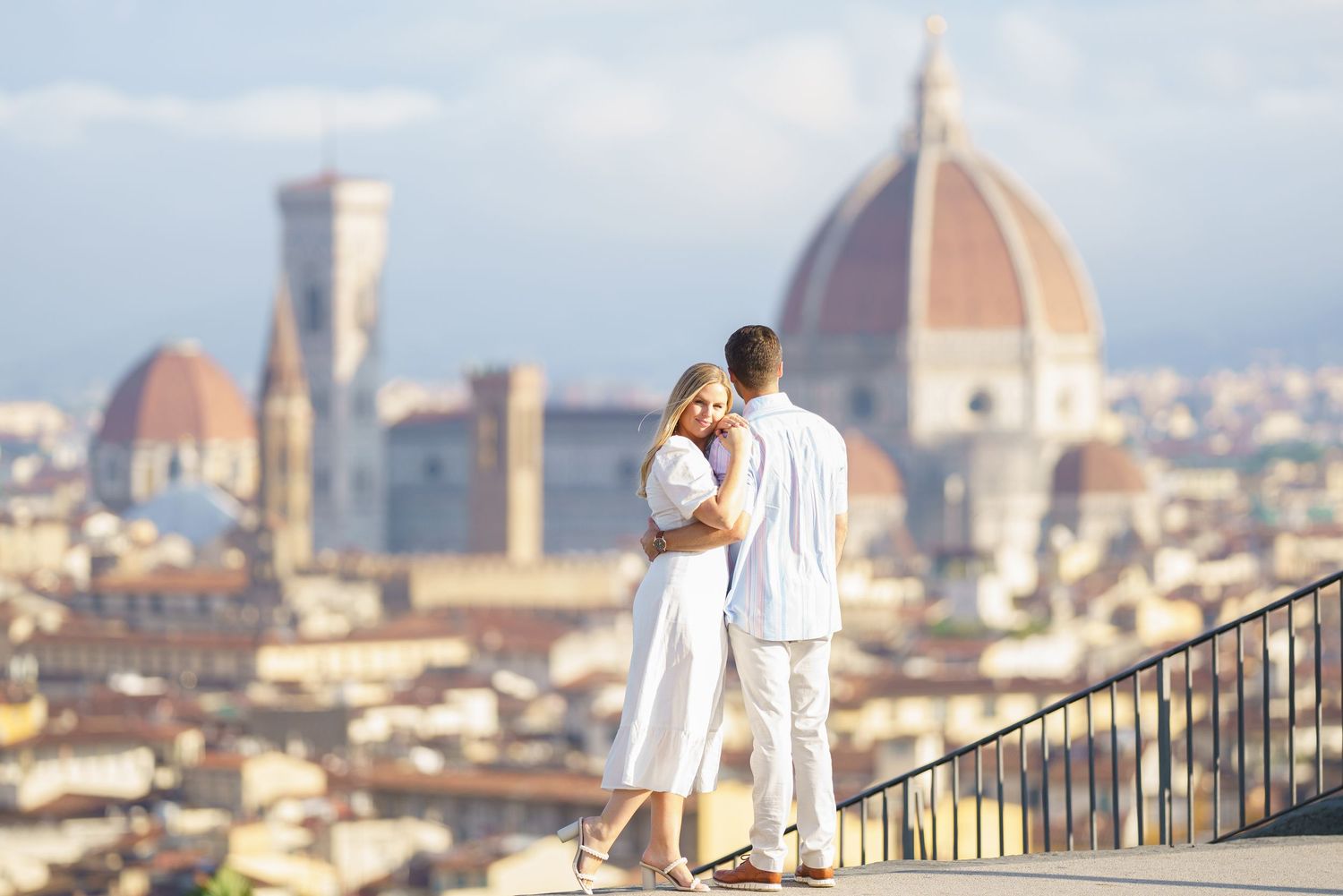 A romantic couple in white outfits admires the stunning Florence cityscape with its iconic Duomo cathedral in the background.