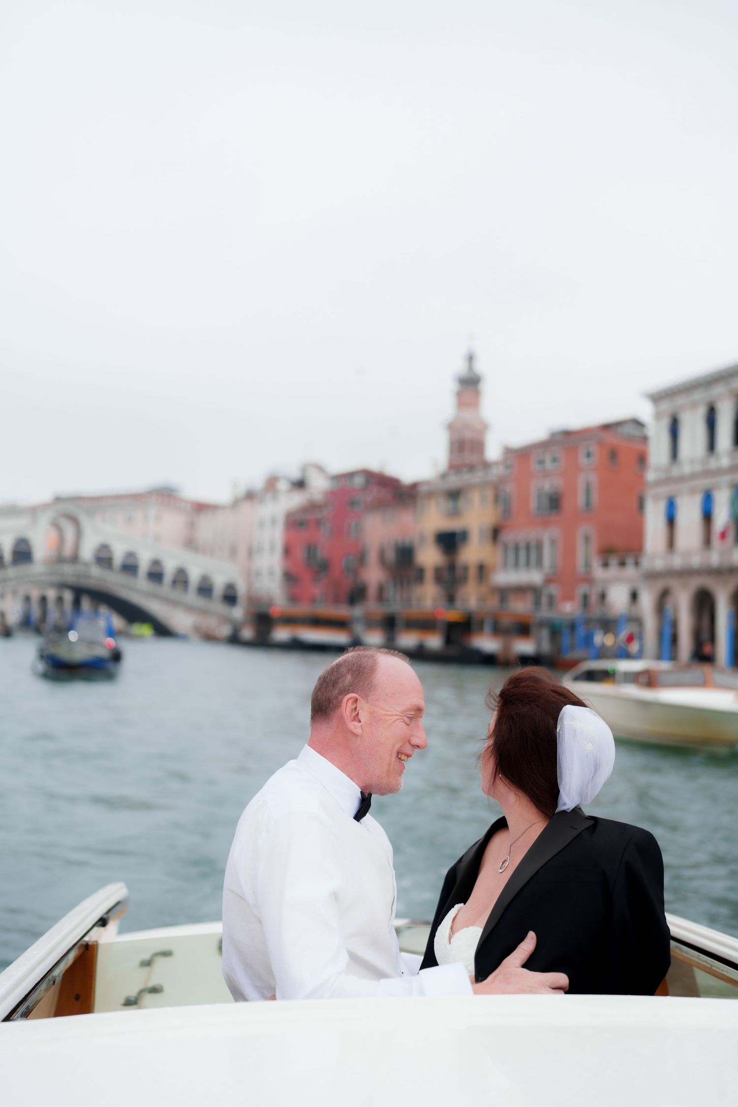 Romantic couple shares intimate moments while riding in a gondola along Venice's scenic canals with colorful buildings behind.