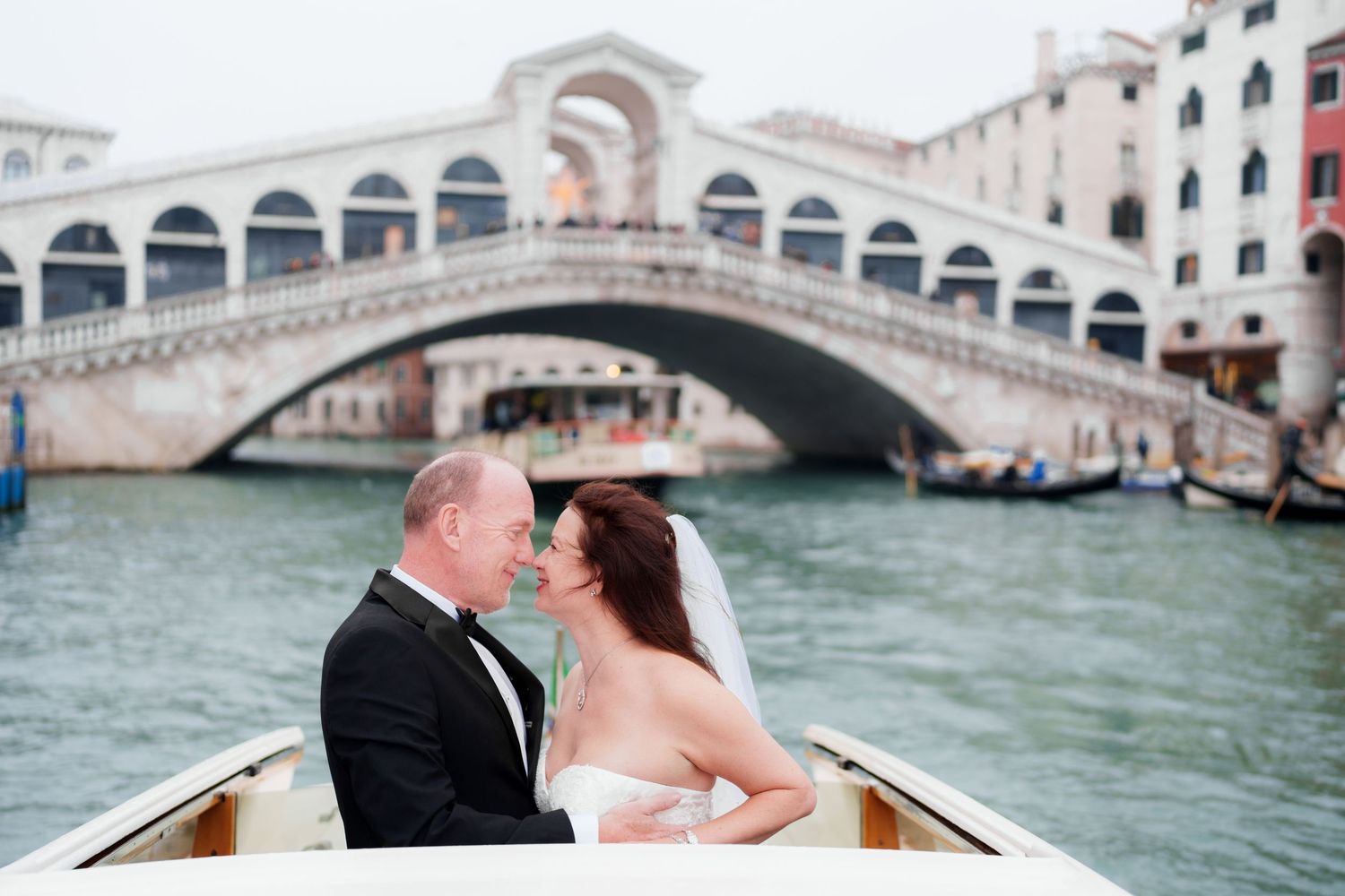 A romantic couple shares an intimate moment while riding in a gondola along Venice's iconic canals near the Rialto Bridge.