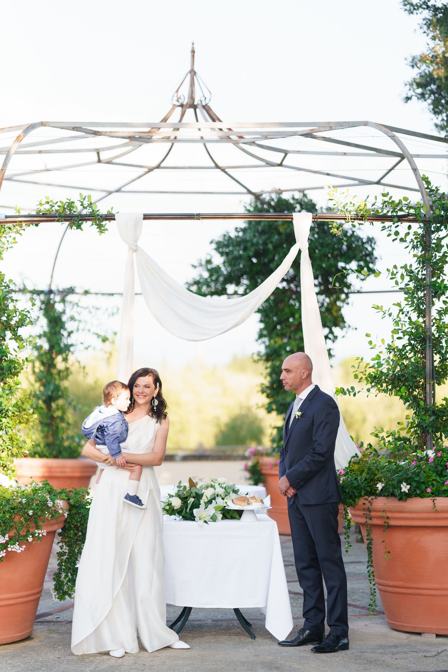 Wedding celebration in garden setting with white fabric canopy and decorative potted plants.