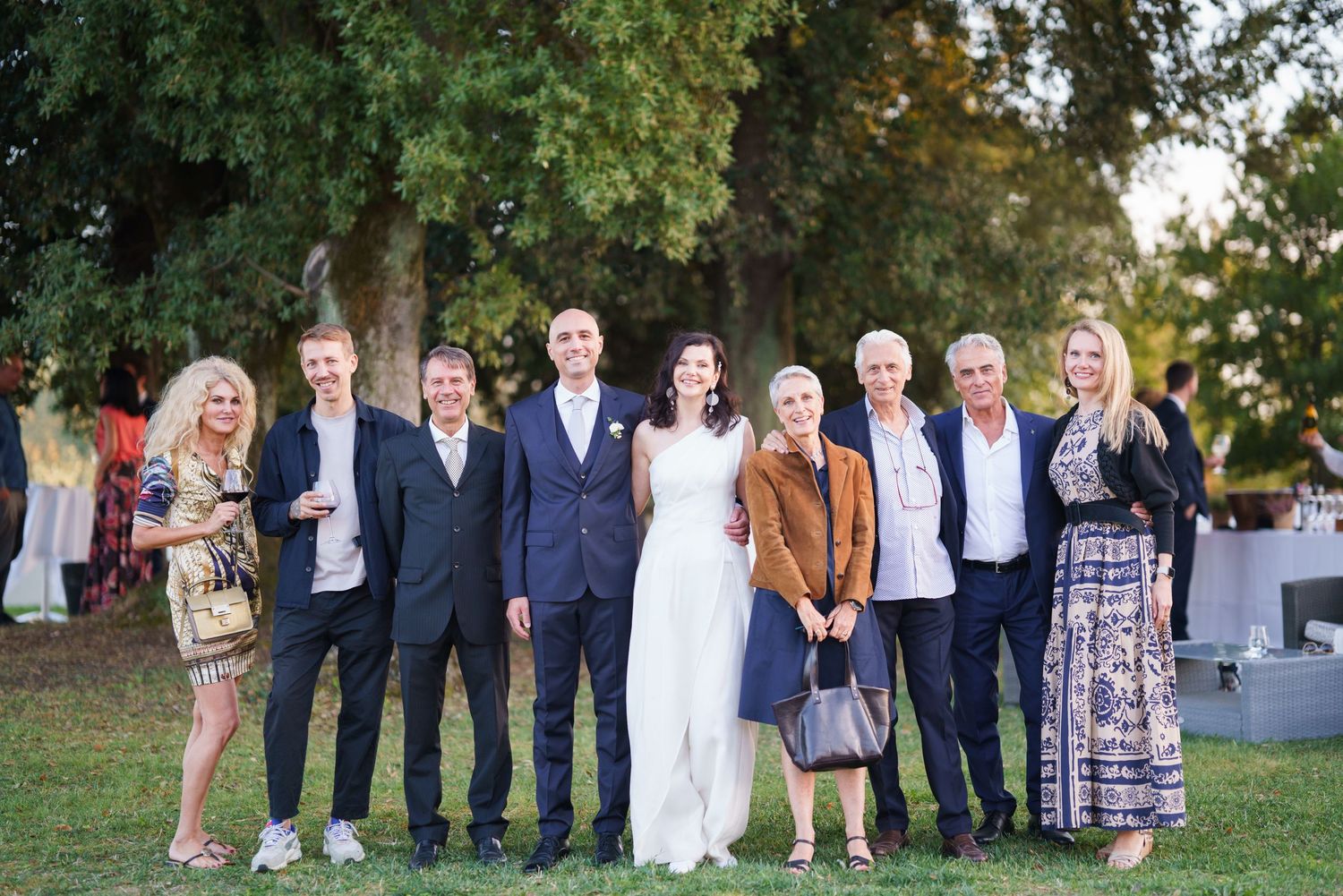 Extended family and wedding guests gather for group photo outdoors.