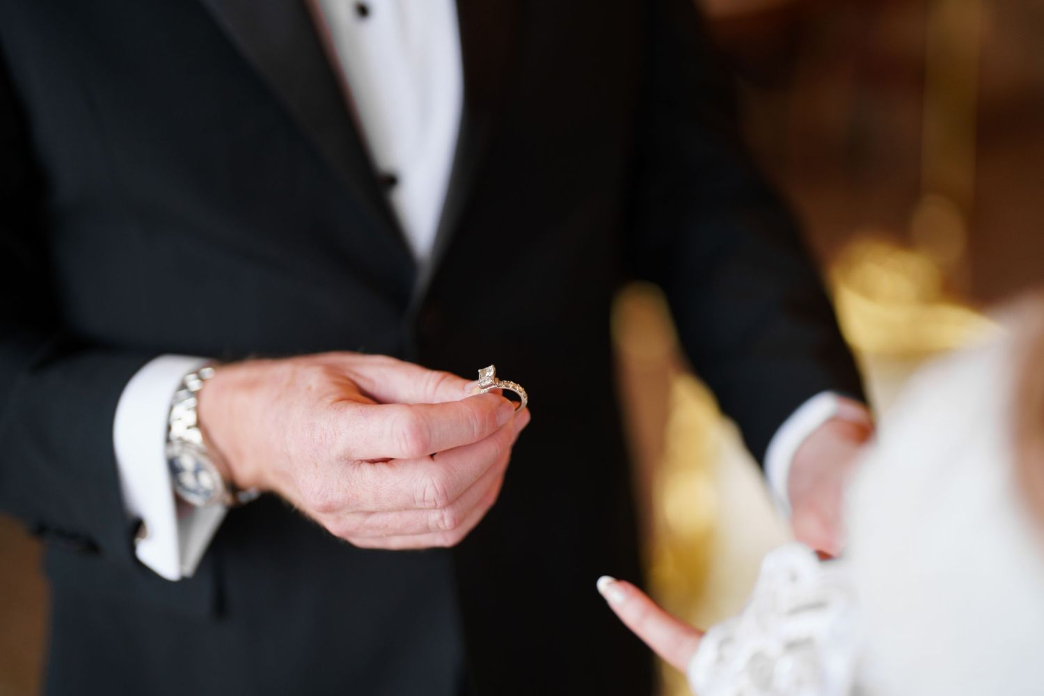 Close-up detail of hands exchanging wedding rings during an elegant marriage ceremony.