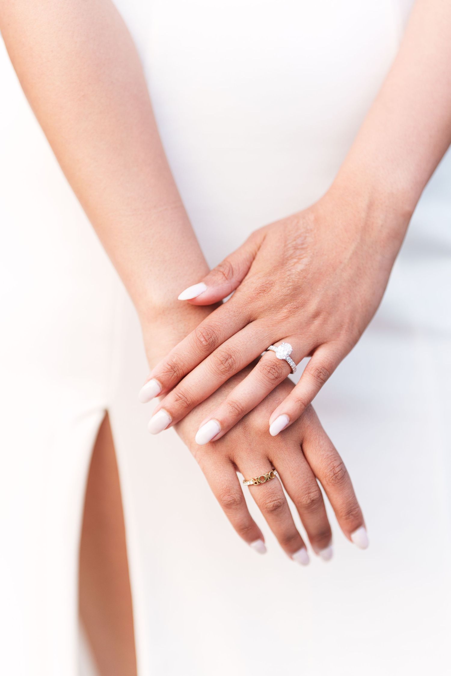 Close-up of hands showing engagement ring and wedding band on white background.
