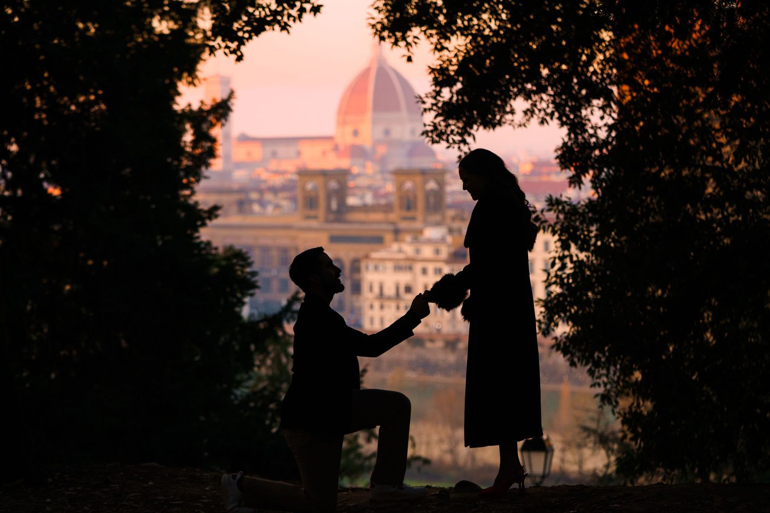 Silhouetted couple shares romantic proposal moment at sunset overlooking Florence Cathedral in Italy.