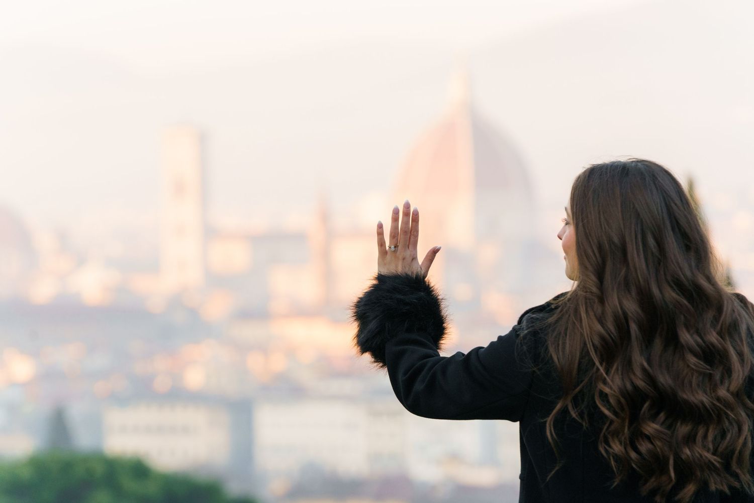 A group of people stand in silhouette against a bright sunset sky, with one person waving their hand.