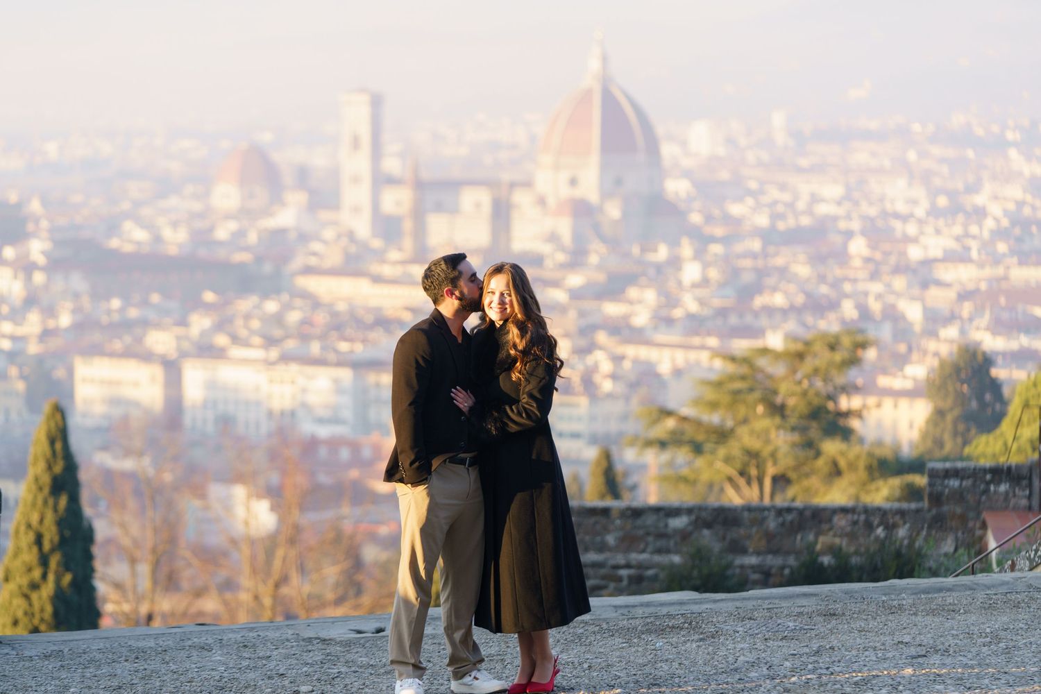 Two people admire the scenic cityscape view from a hilltop overlook at sunset.