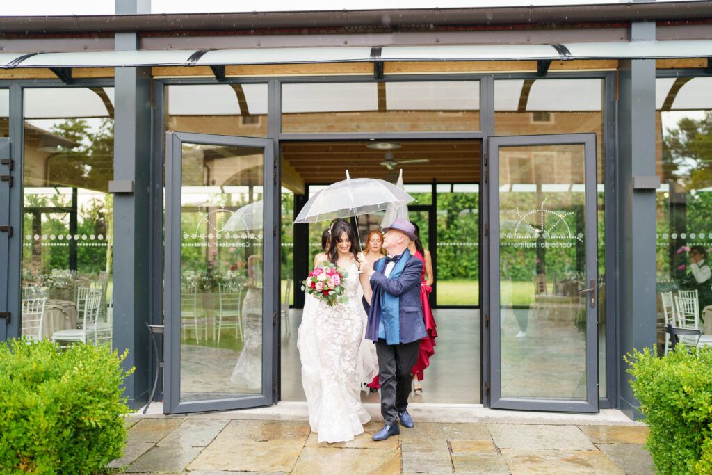 Wedding party photos taken under a modern glass-enclosed walkway surrounded by gardens.