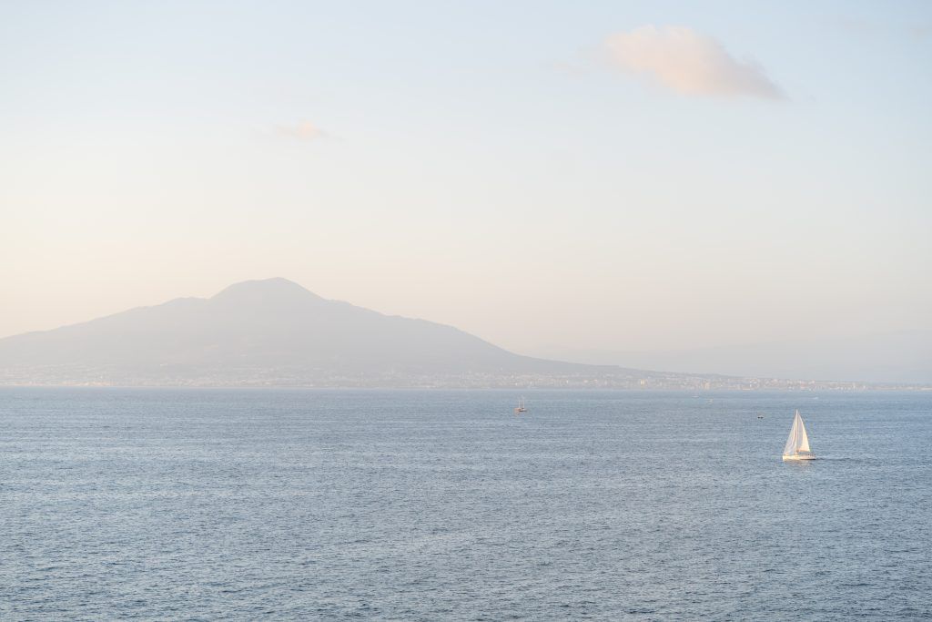 Serene Mediterranean seascape with distant mountains and a sailboat on the horizon.