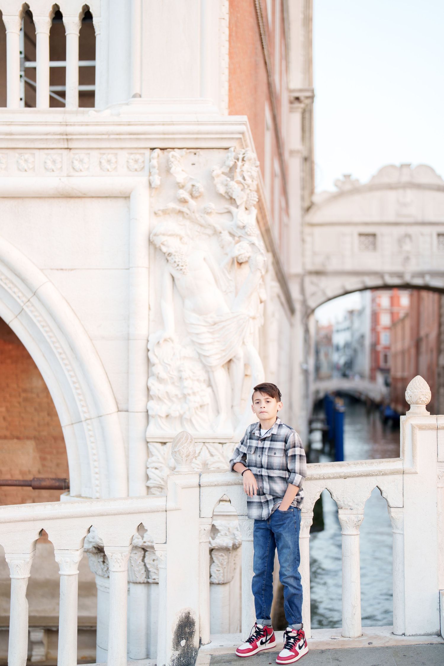 A person stands under ornate white stone arches along a Venetian canal in Italy.