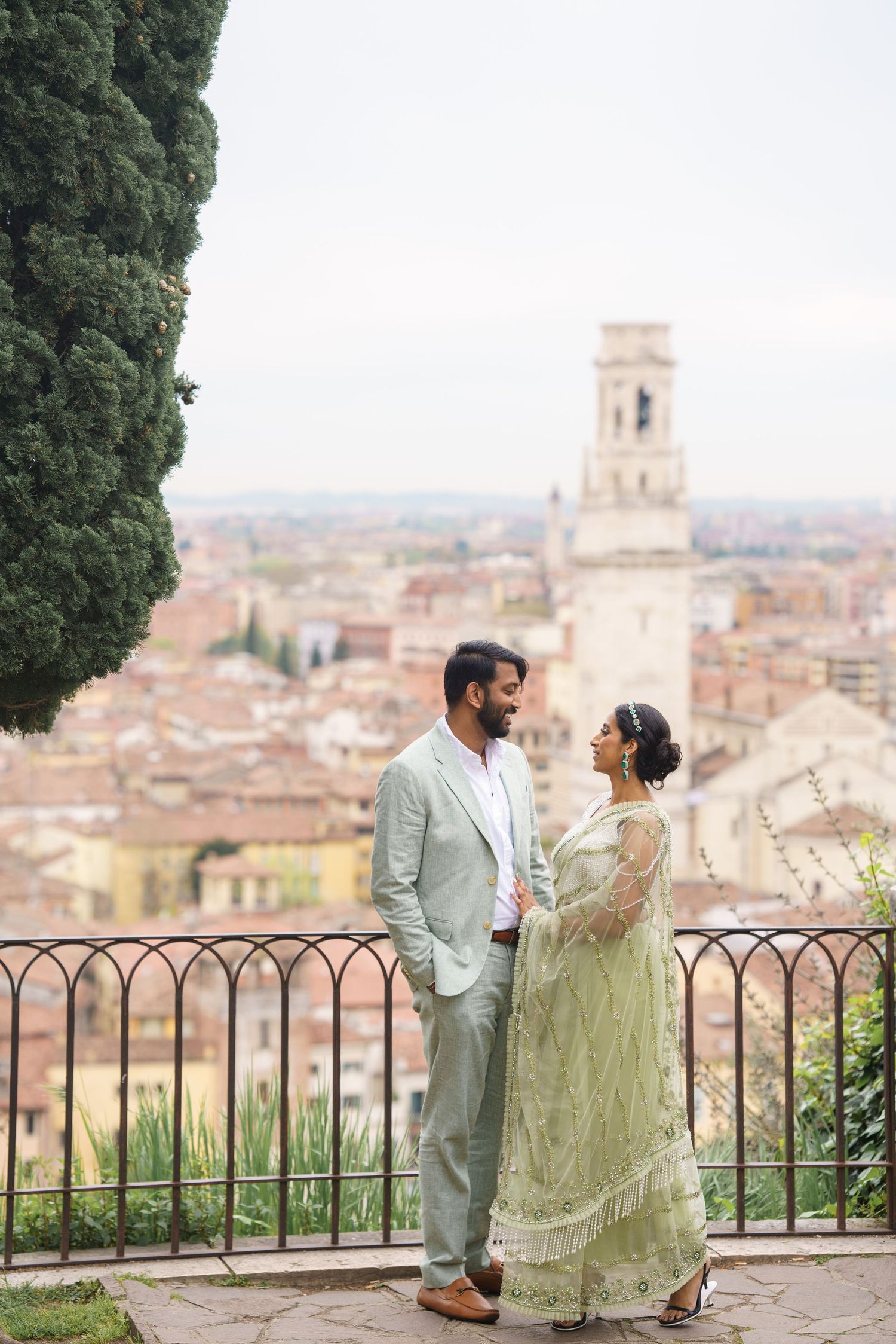Couple enjoying a romantic moment at a scenic overlook with historic Italian architecture and bell tower in the background.