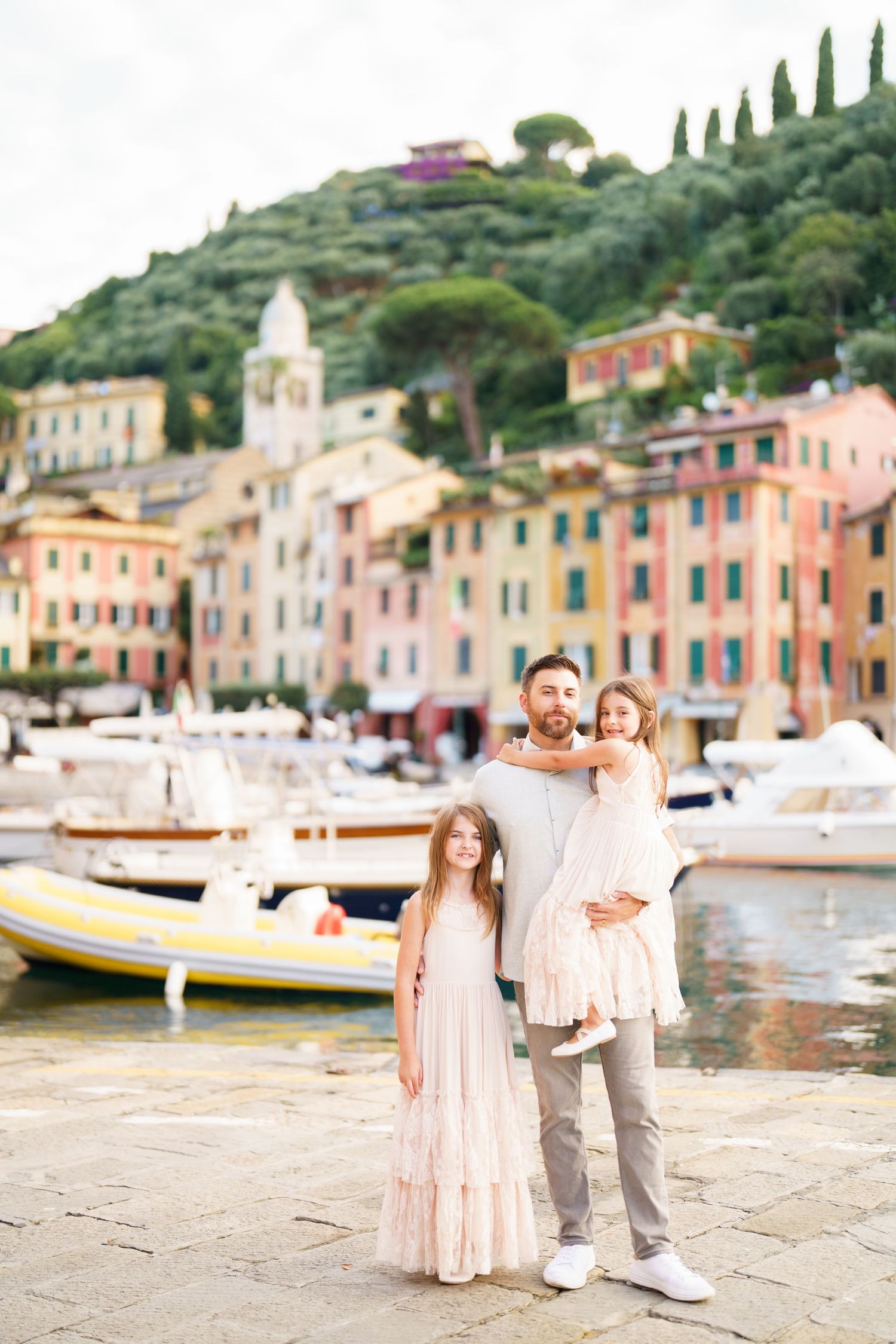 Scenic view of colorful buildings and boats along the waterfront in Portofino, Italy with cypress trees on hillside.