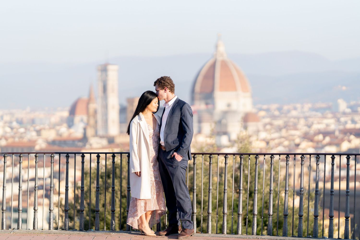 Romantic couple shares a tender moment at a scenic overlook with Florence's iconic Duomo cathedral in the background.