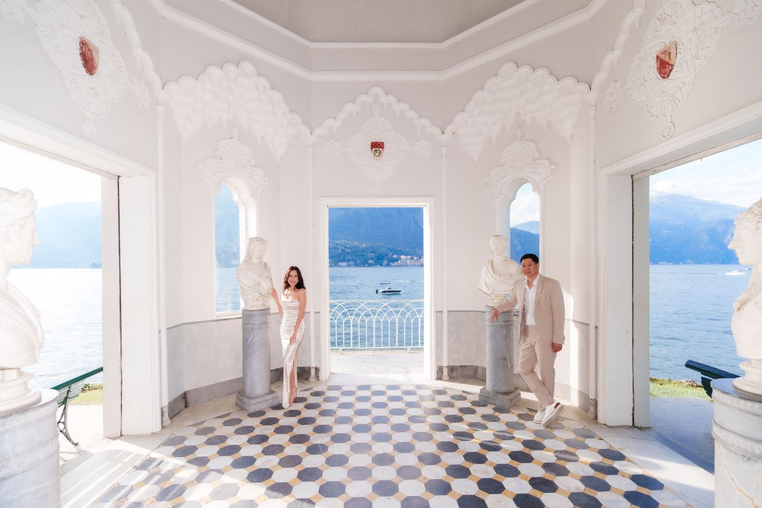 A bright white room with checkerboard floors and large windows overlooks a scenic coastal mountain landscape.