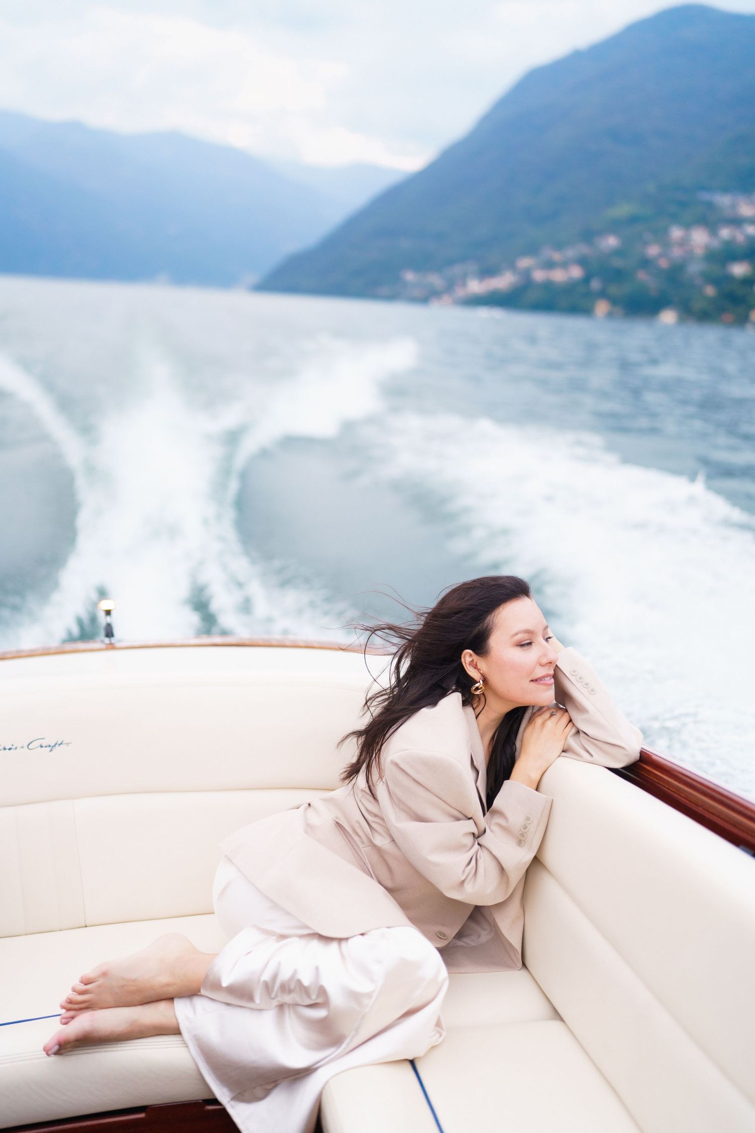 Woman relaxing on white leather boat seats with mountains and lake in background on sunny day.
