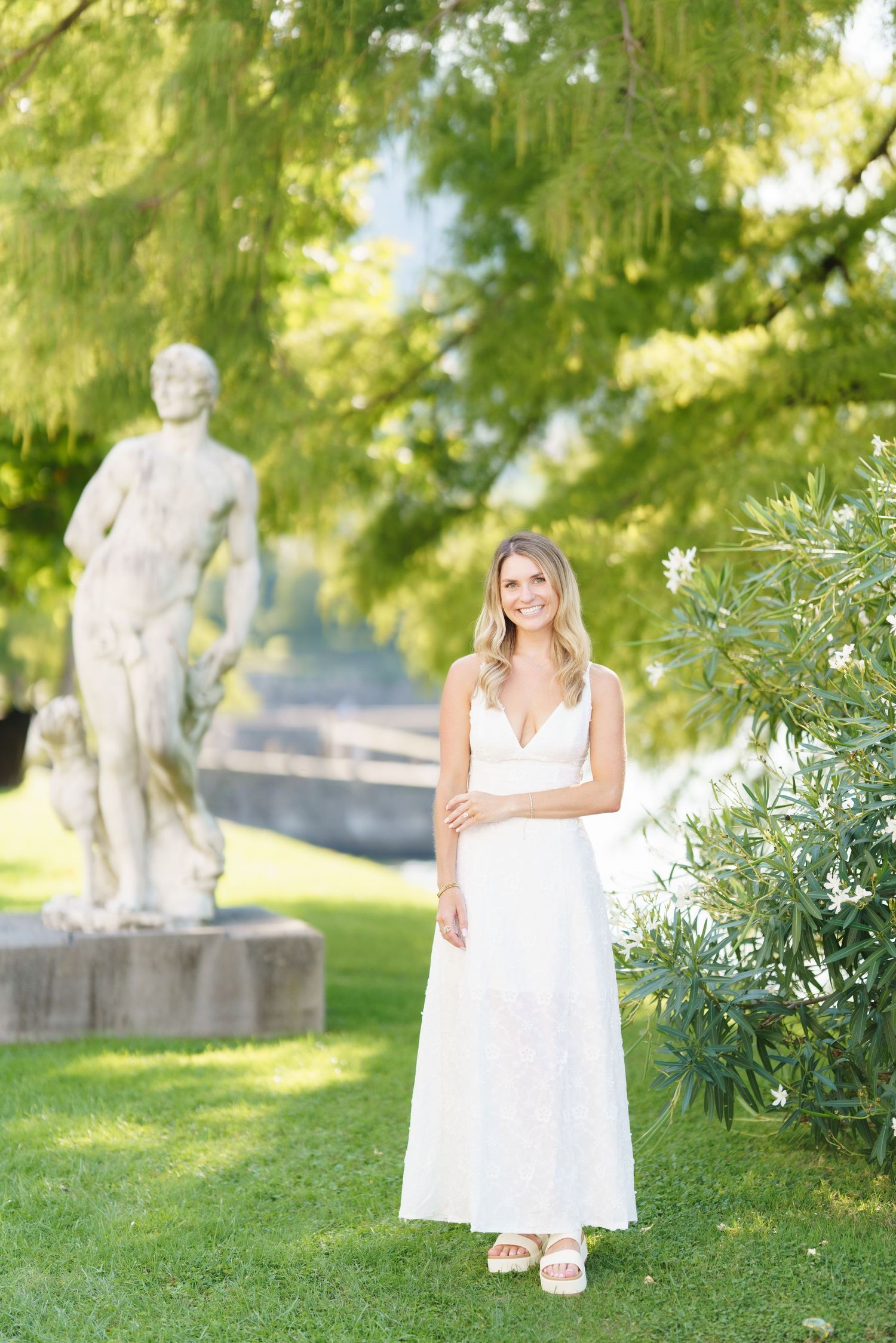 A white maxi dress worn in a garden setting with a classical stone statue in the background.
