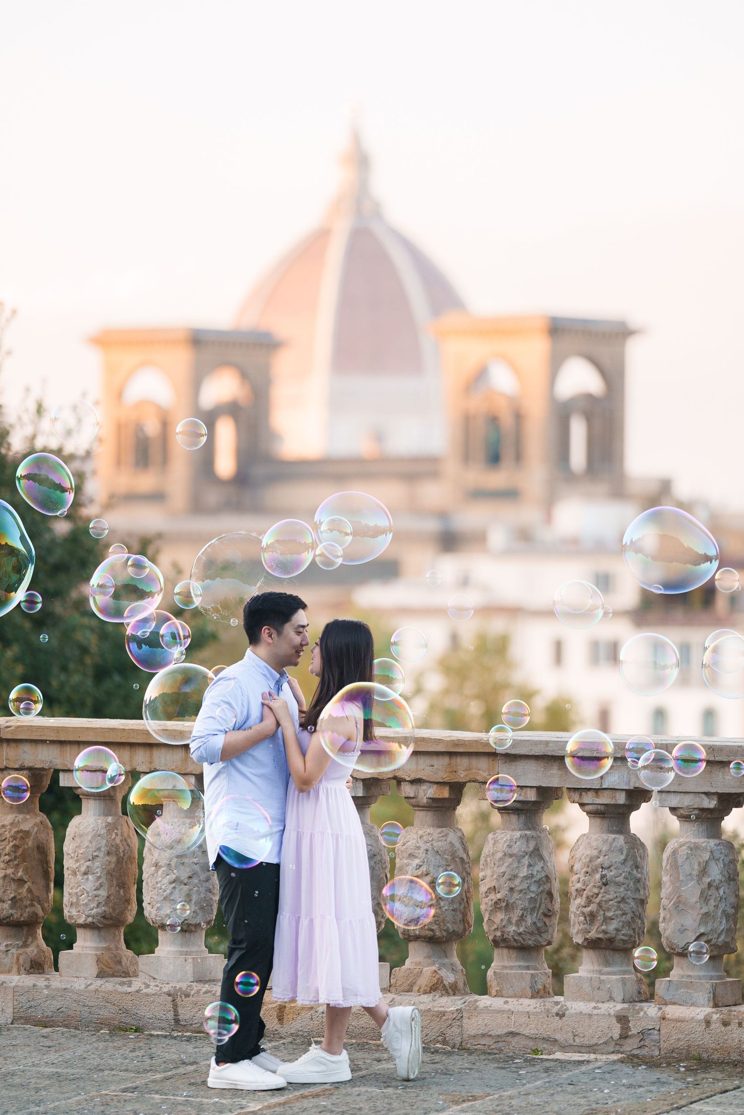 Romantic couple shares tender moments on a stone balcony with soap bubbles floating in the sunset light at a castle.