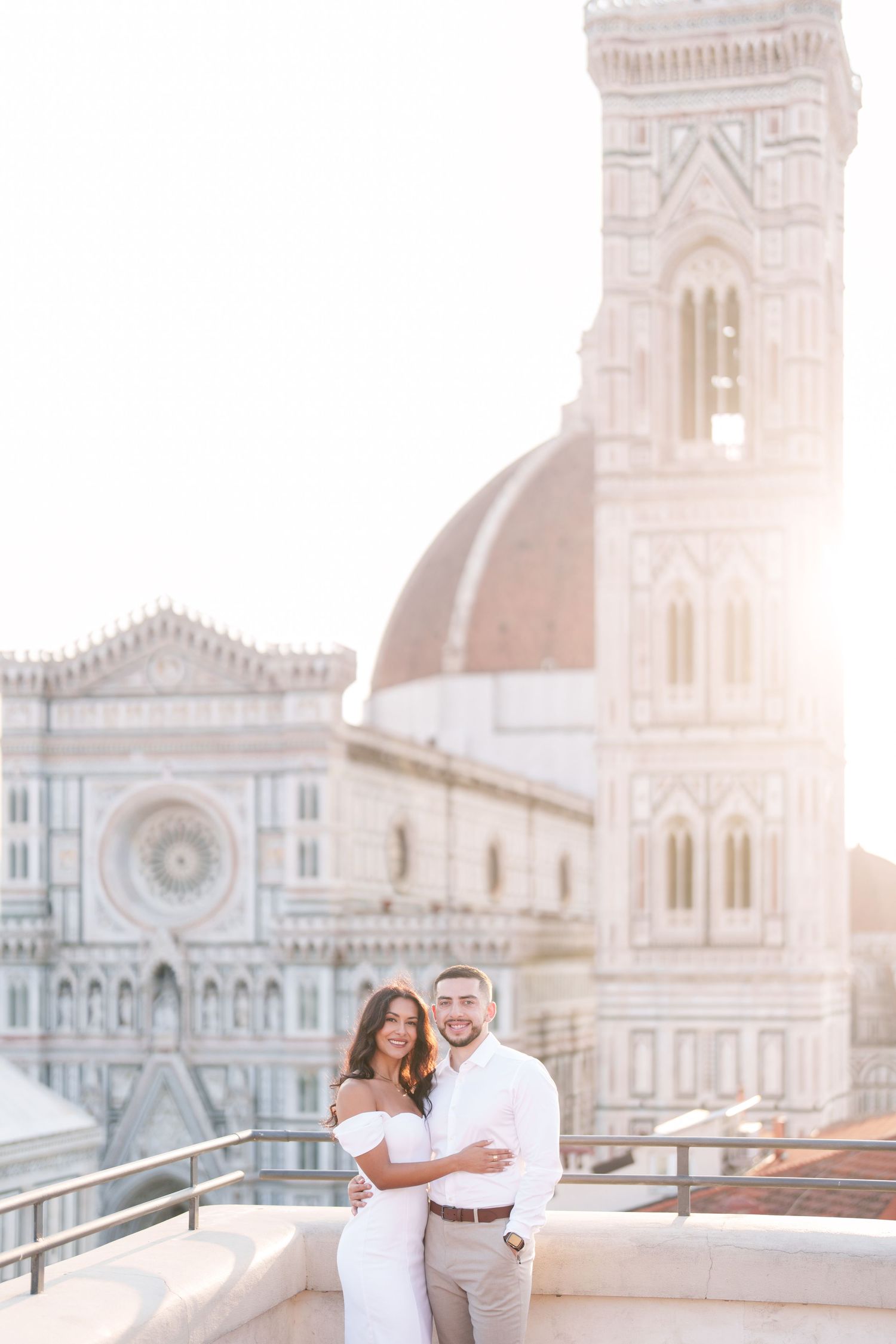 Romantic couple embraces on rooftop terrace overlooking Florence Cathedral during golden sunset hour.